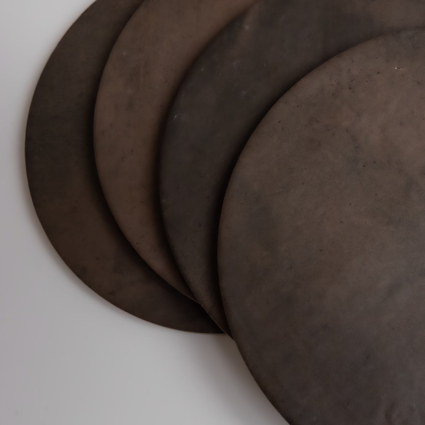 Four overlapping round, dark brown Finca Ocre Extra Sample metal disks on a light background, viewed from above.