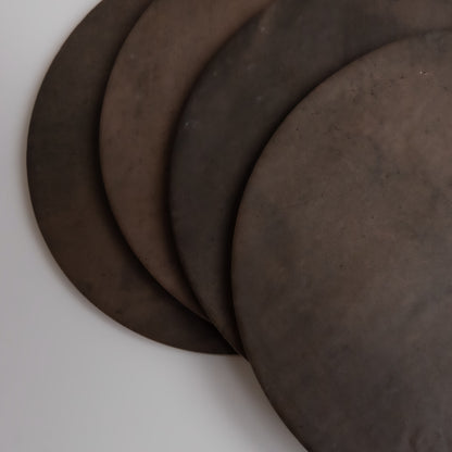 Four overlapping round, dark brown Finca Ocre Extra Sample metal disks on a light background, viewed from above.
