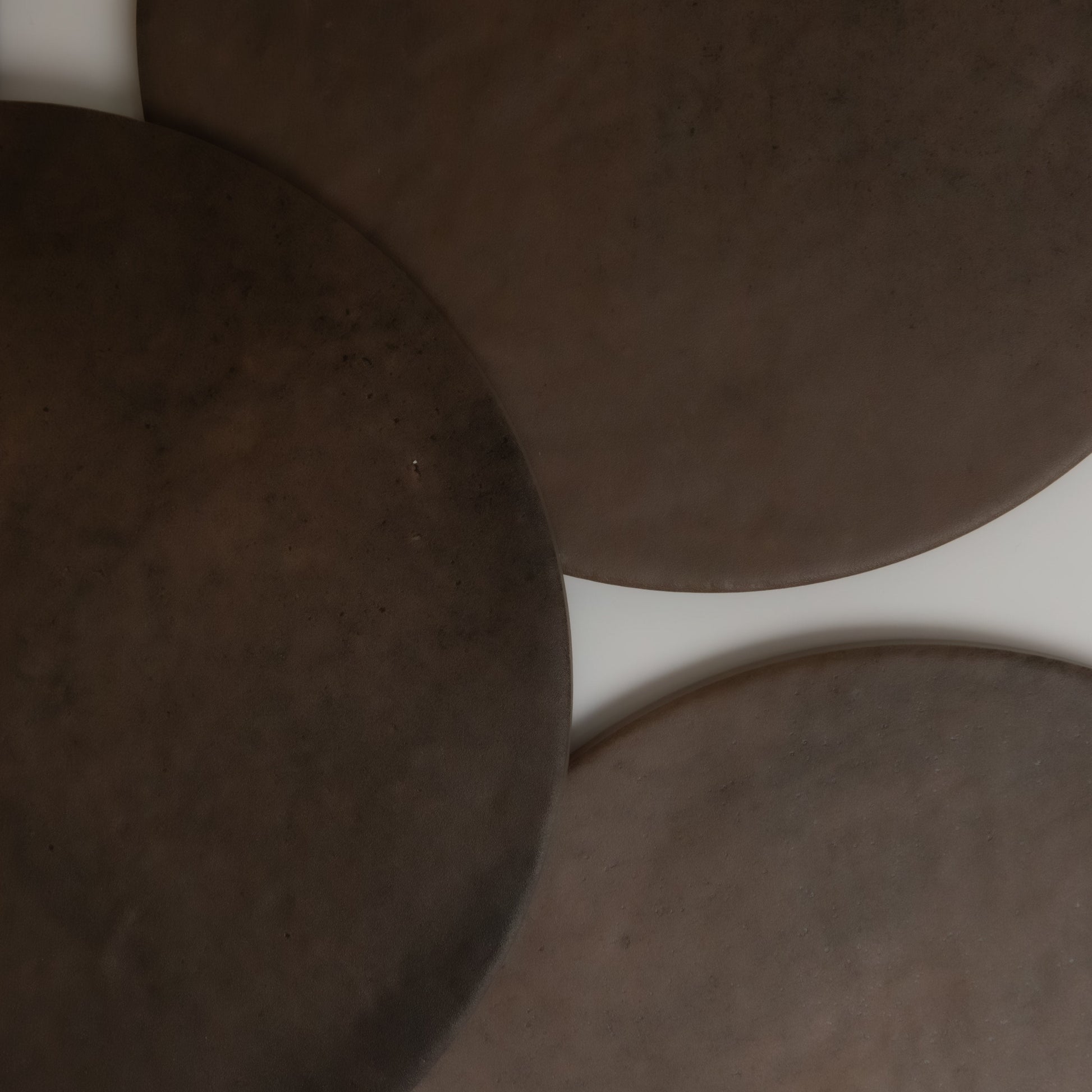 Three overlapping, round, dark brown Finca Ocre Extra Sample surfaces on white, resembling ceramic or stone plates.