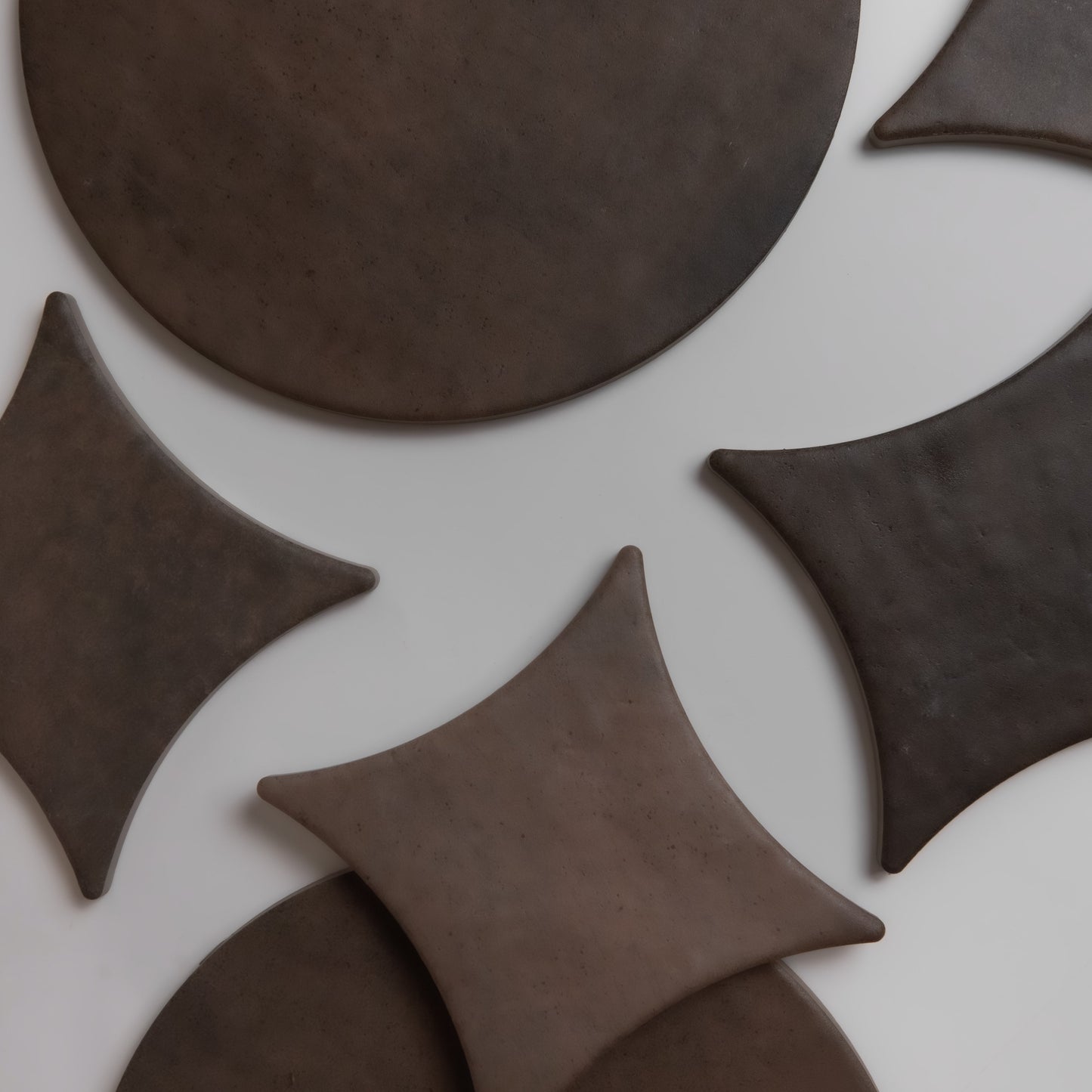 Overhead view of Finca Ocre, Extra Sample round and diamond dark brown ceramic tiles on a white surface.