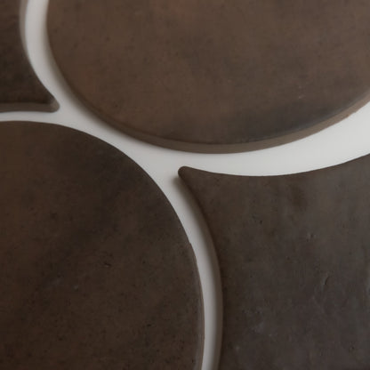 Close-up of Finca’s Ocre, Extra Sample: overlapping dark brown ceramic shapes on a white surface.