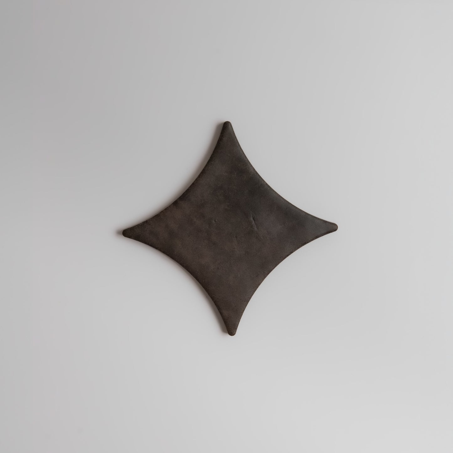 A dark, diamond-shaped Ocre, Extra Sample by Finca rests on a plain, light gray background.