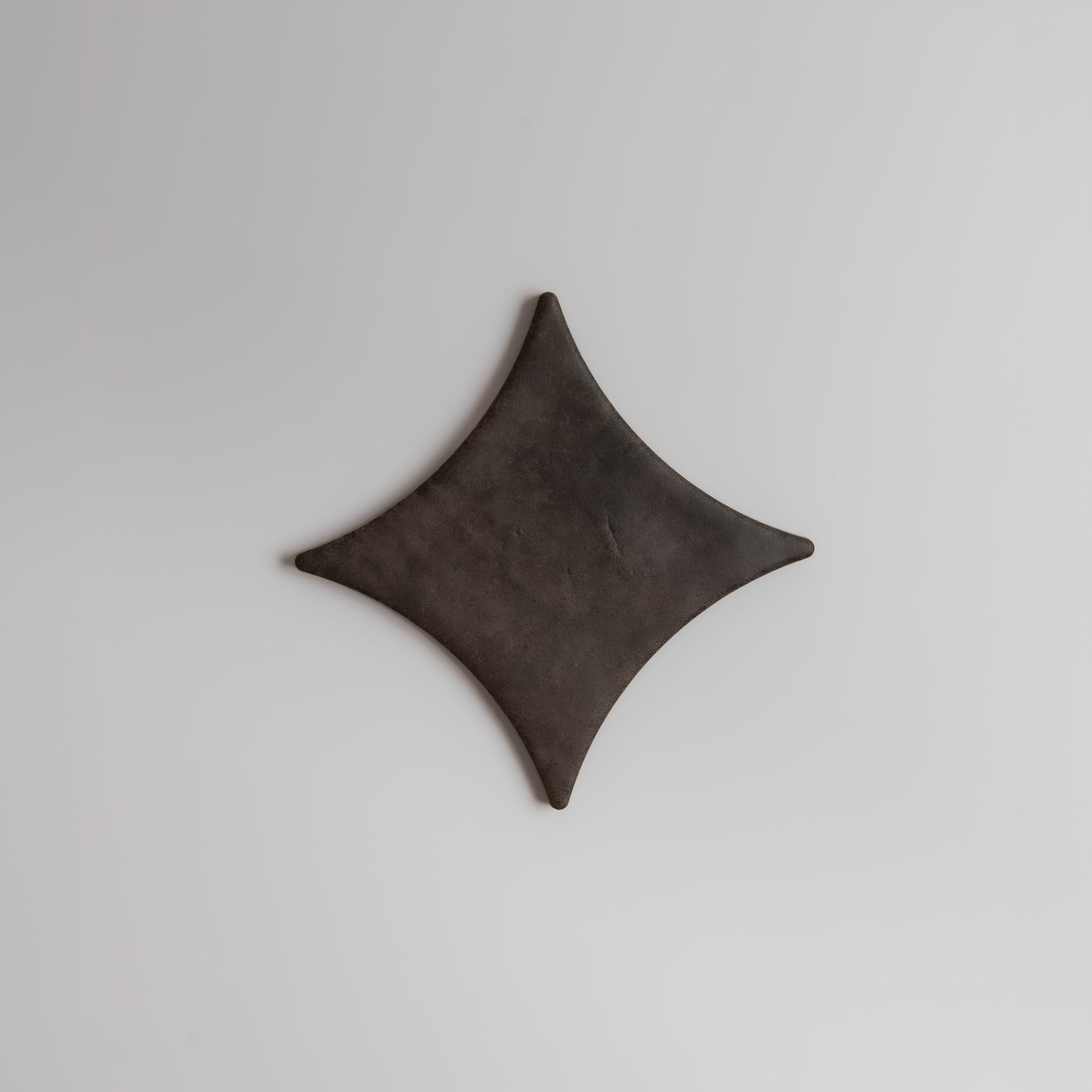 A dark, diamond-shaped Ocre, Extra Sample by Finca rests on a plain, light gray background.