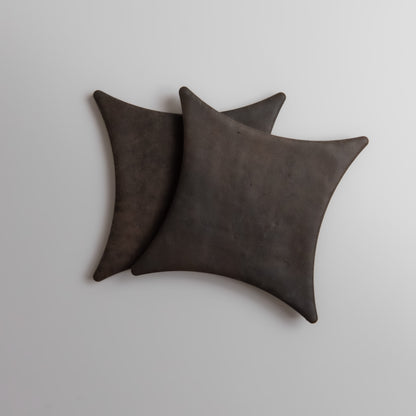 Two overlapping, square Ocre, Extra Sample pillows by Finca on a light surface; dark brown with pointed corners.