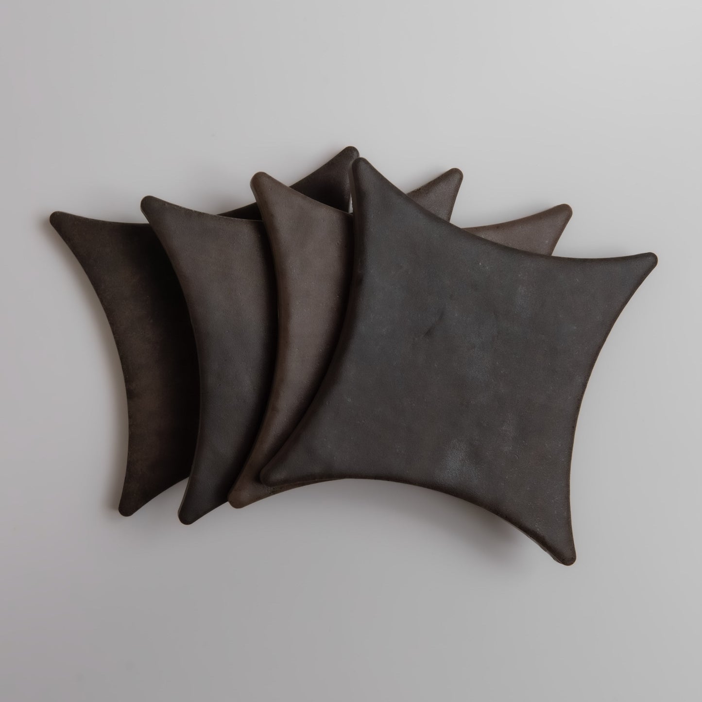 Four overlapping, dark, curved square shapes from Finca's Ocre, Extra Sample on a light background.