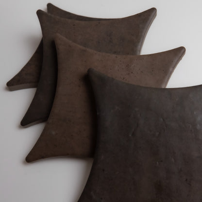 Four dark, triangular Ocre, Extra Sample ceramic plates by Finca, stacked on a white background.
