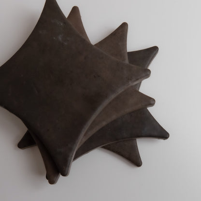 Four Ocre, Extra Sample objects by Finca, star-shaped and dark, stacked and slightly overlapping on a white surface.