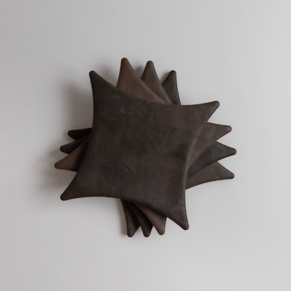 Five dark, square Ocre, Extra Sample plates by Finca with pointed corners stacked on a white surface.
