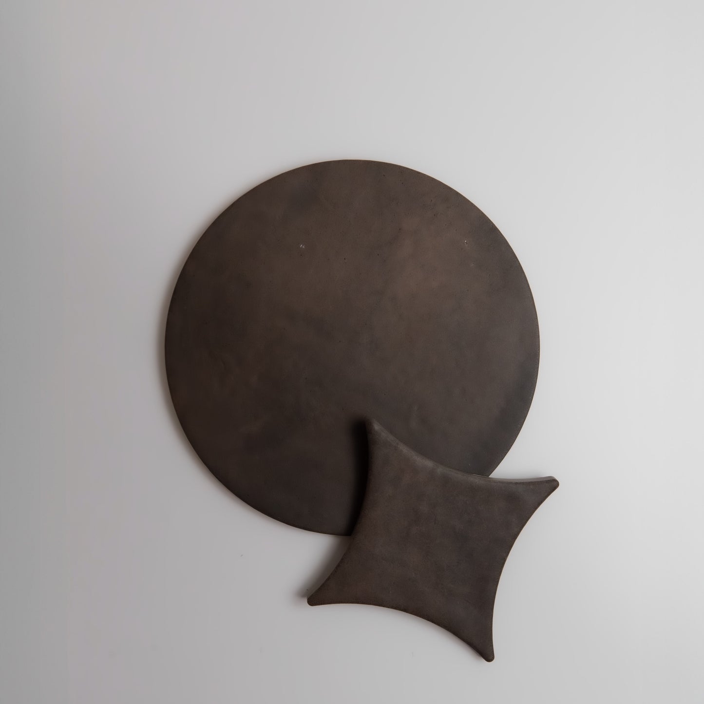 Finca Ocre Extra Sample: dark brown, minimalist round and pointed leather shapes on a plain light background.