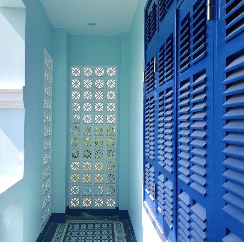 Narrow corridor with patterned floor tiles, blue louvered shutters, and a wall of decorative glass blocks letting in light.