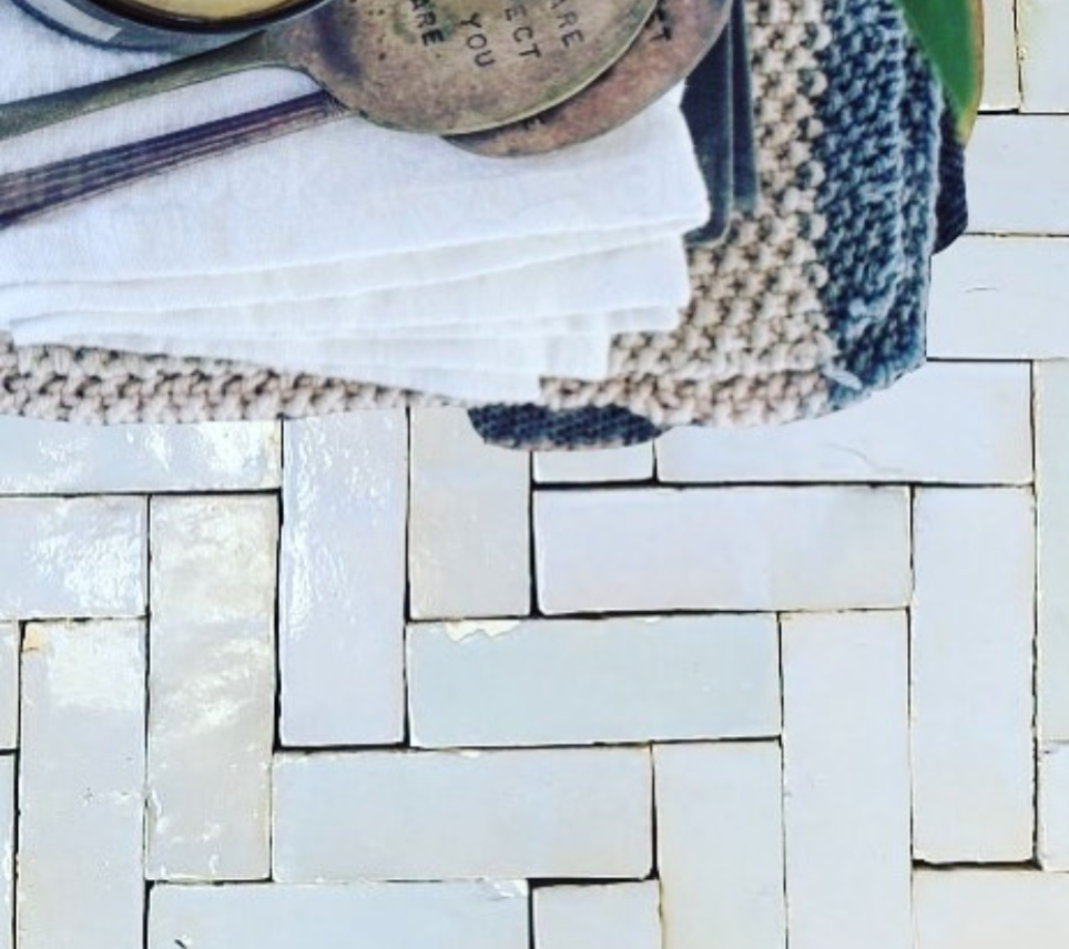 Stack of folded towels with metal measuring spoons on top, set on a textured, light herringbone tile surface.