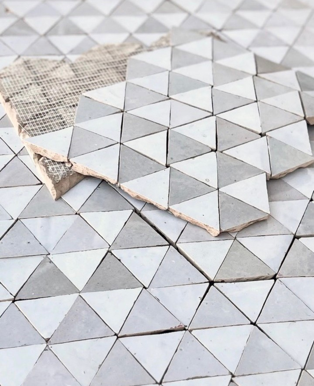 Sheets of triangular gray and white tiles are stacked on a matching tiled surface.