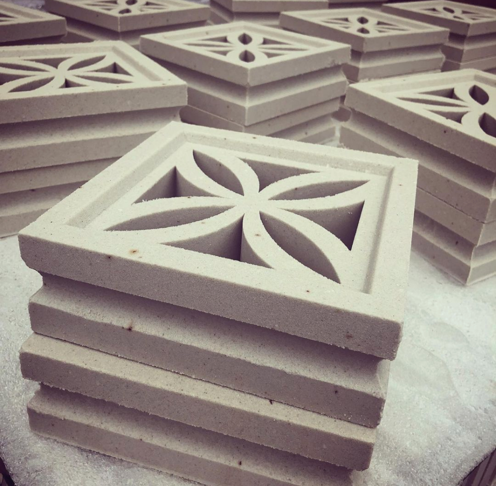 Stacks of square concrete tiles with decorative cut-out flower patterns on a light surface.