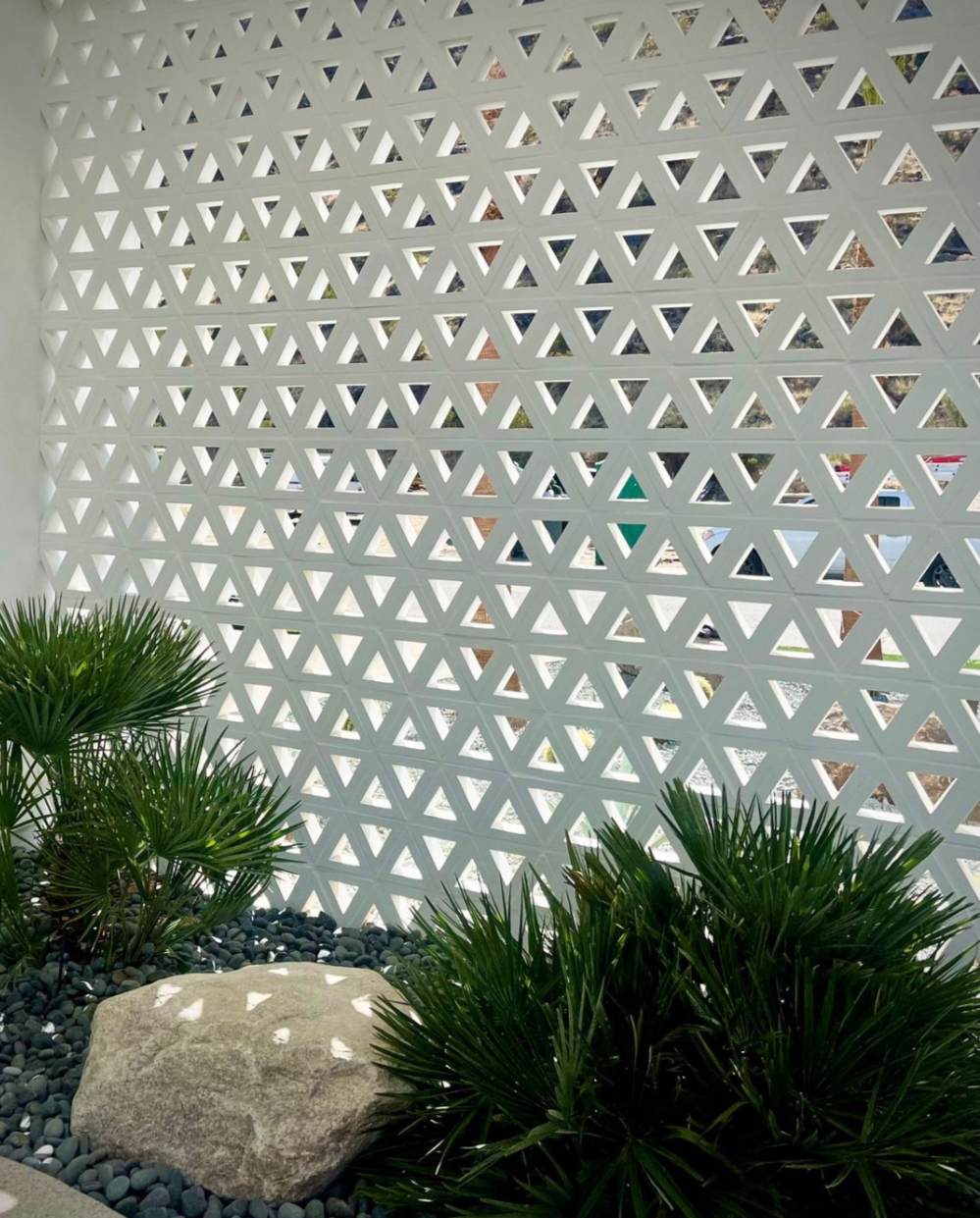 Geometric triangle-patterned wall with green plants and a large rock in a landscaped area.