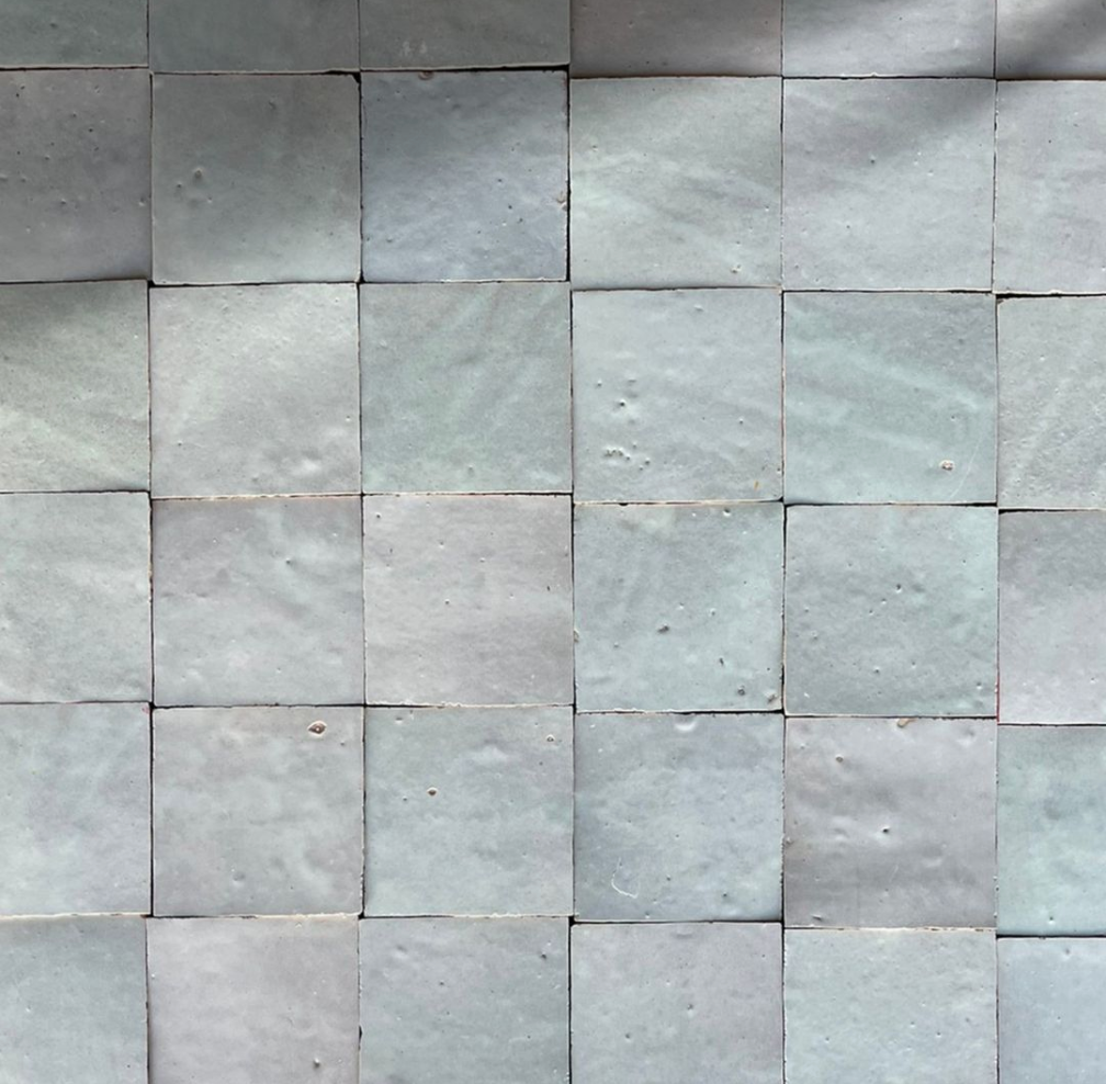 A close-up of a tiled surface with light gray square tiles arranged in a grid pattern.