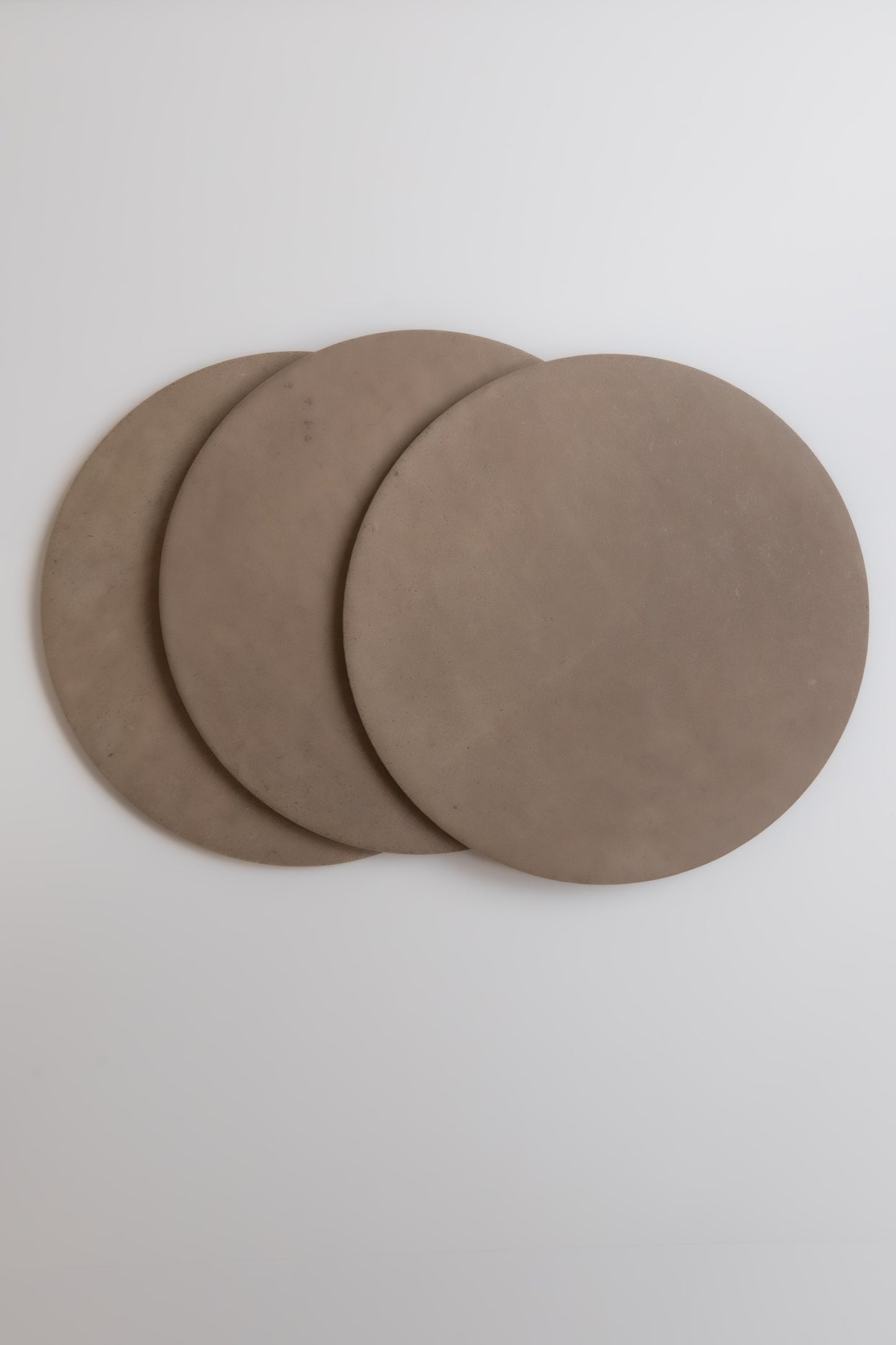Three overlapping round, flat Pampas mats by Finca in brown on a light gray background.