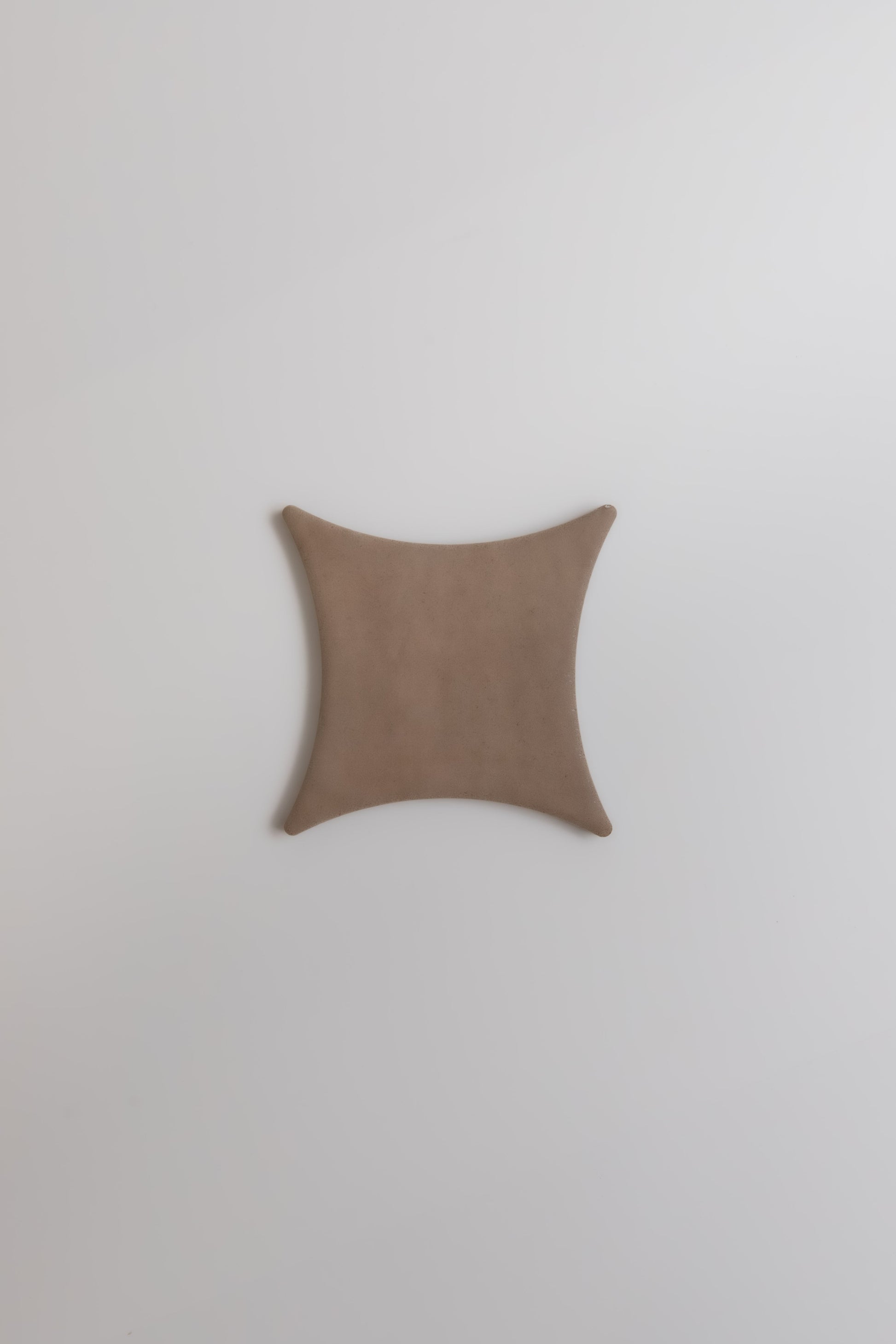 A brown, square-shaped Pampas by Finca with concave sides on a plain white background.
