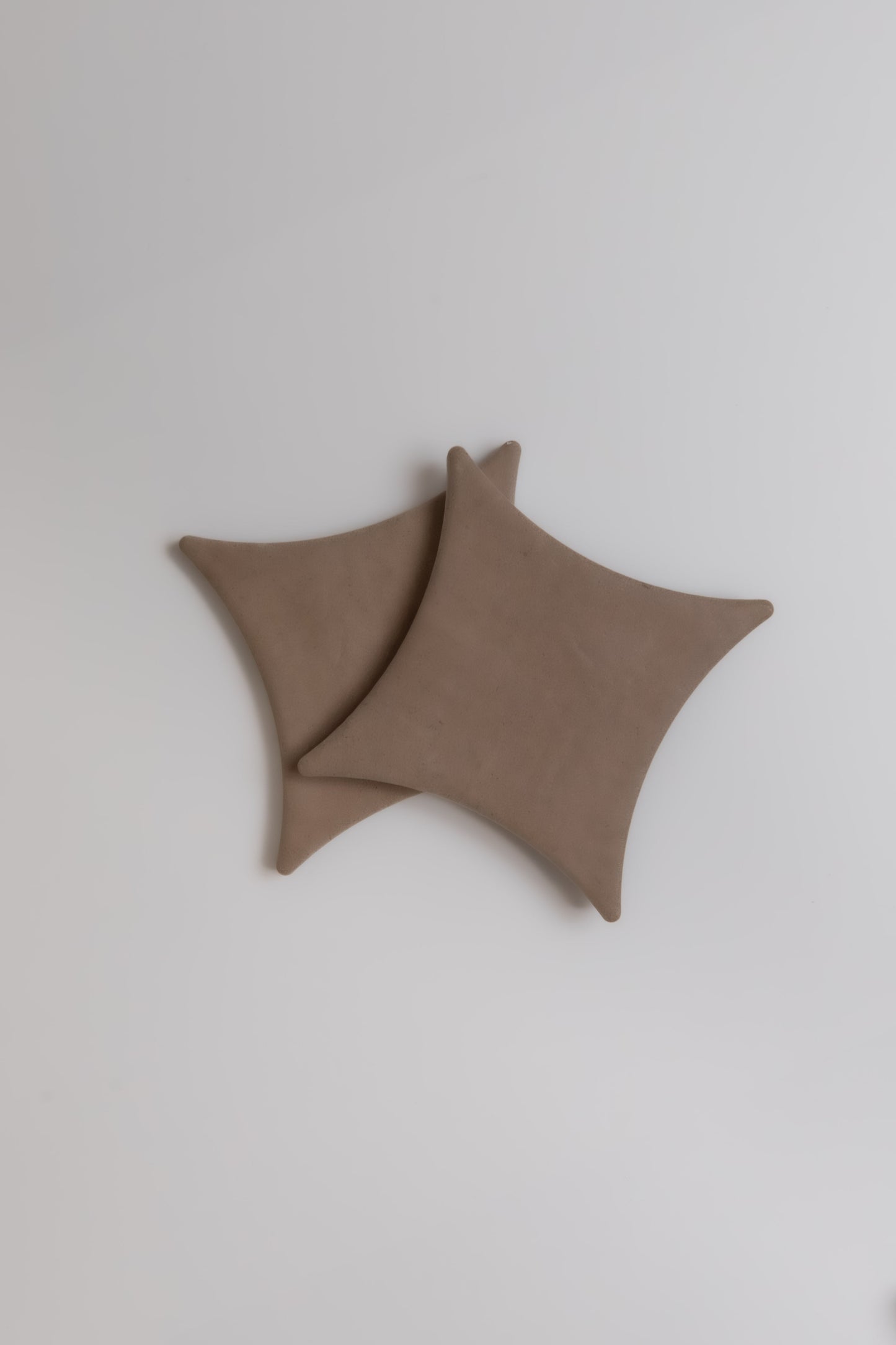 Two overlapping Finca Pampas square brown coasters with rounded corners on a plain white surface.