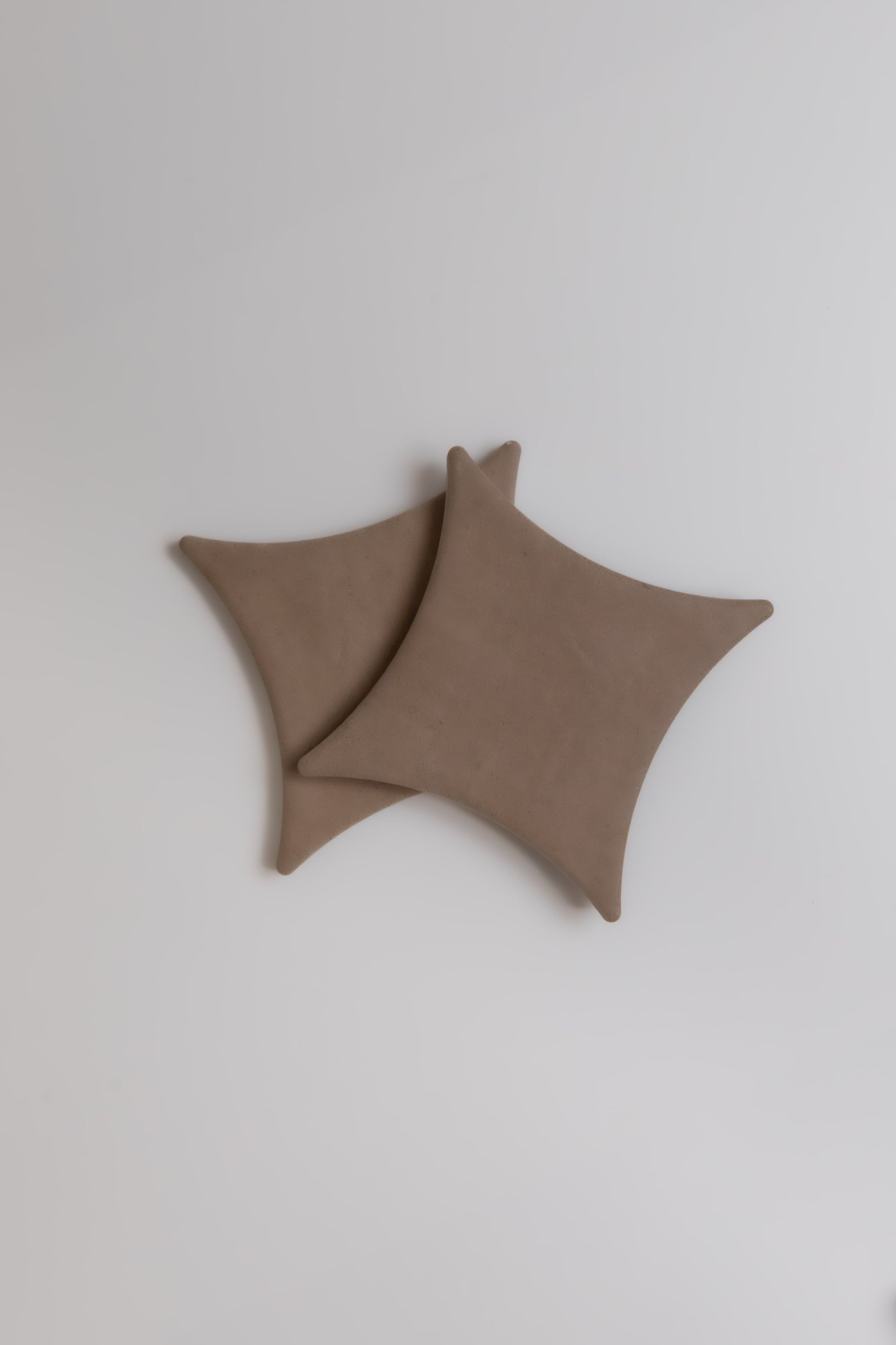 Two overlapping Finca Pampas square brown coasters with rounded corners on a plain white surface.