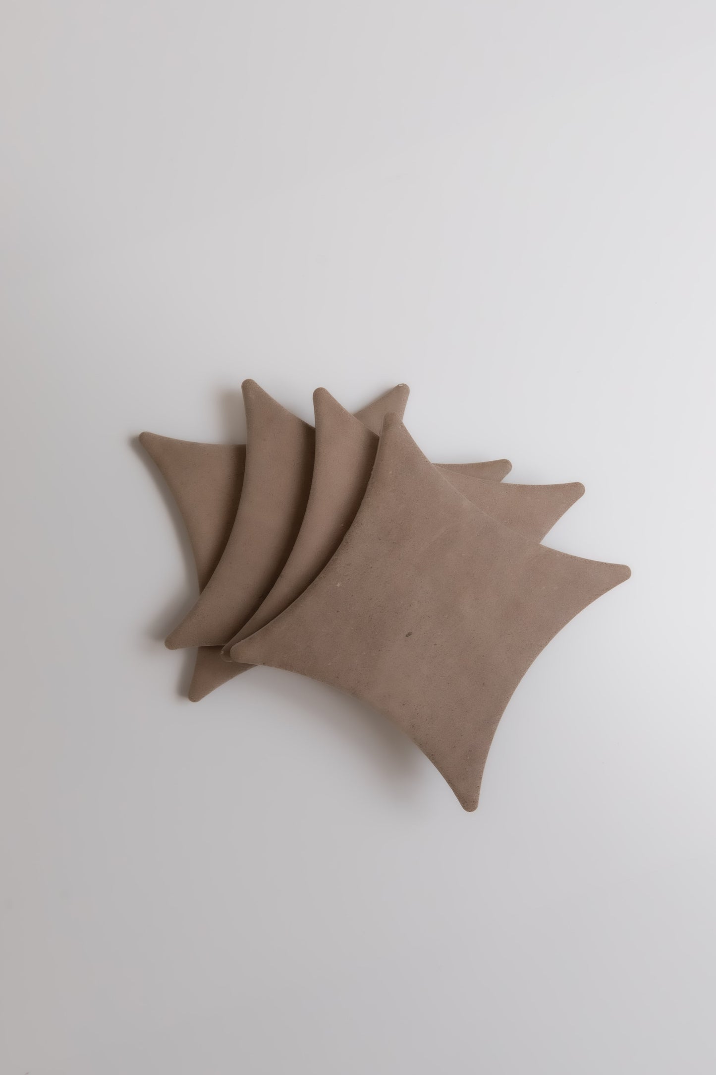 Four brown Pampas coasters by Finca, square with rounded corners, overlap on a white surface.