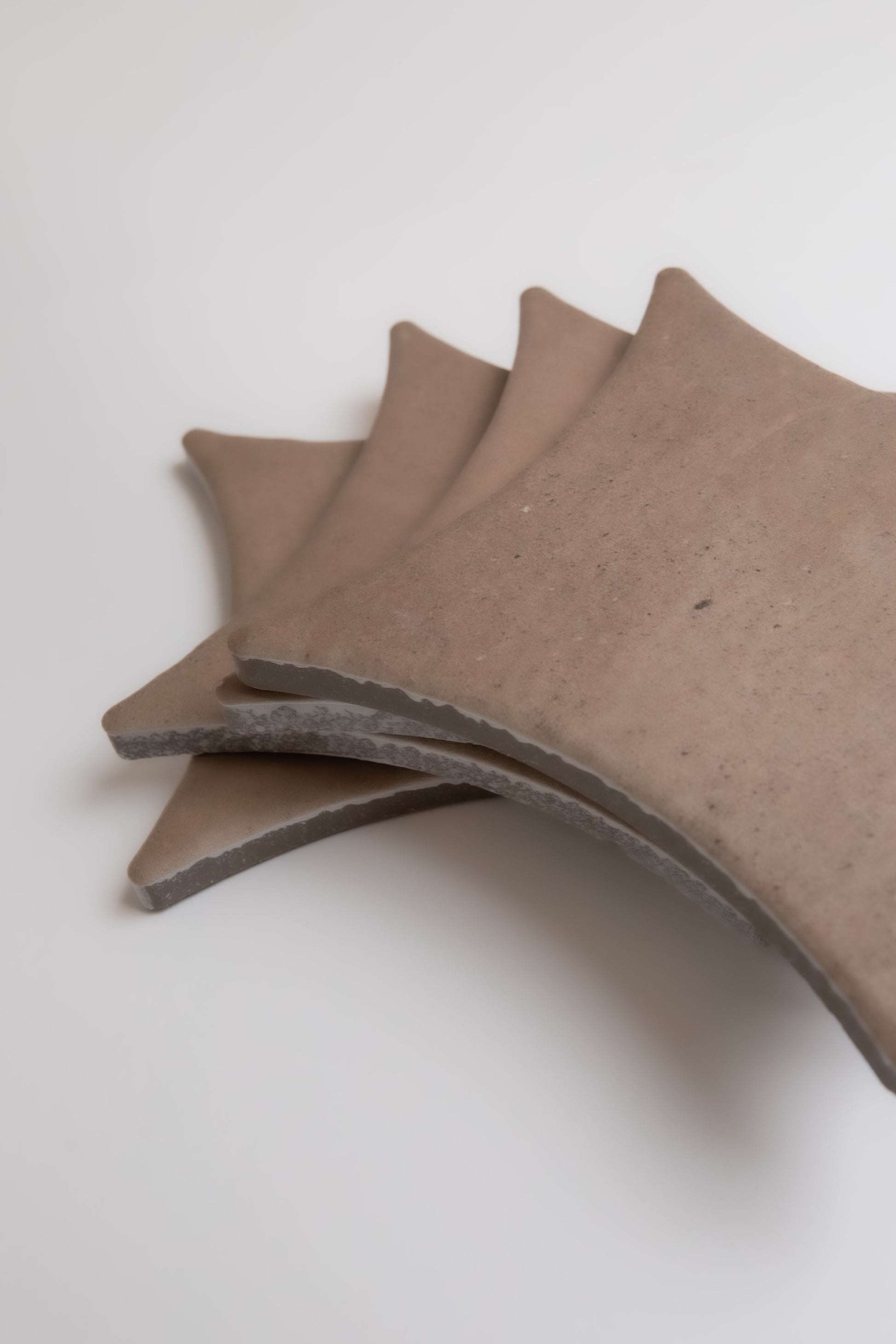 Four brown, fan-shaped Pampas ceramic tiles by Finca overlap each other on a white surface.