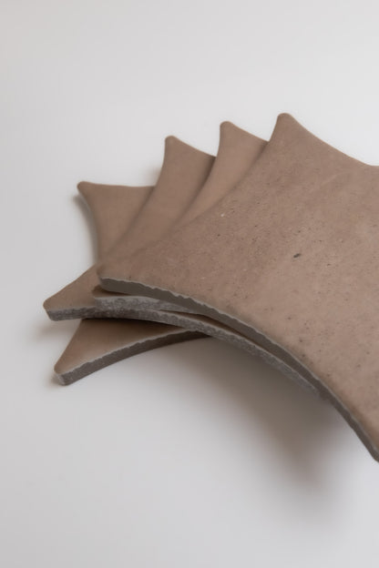 Four brown, fan-shaped Pampas ceramic tiles by Finca overlap each other on a white surface.