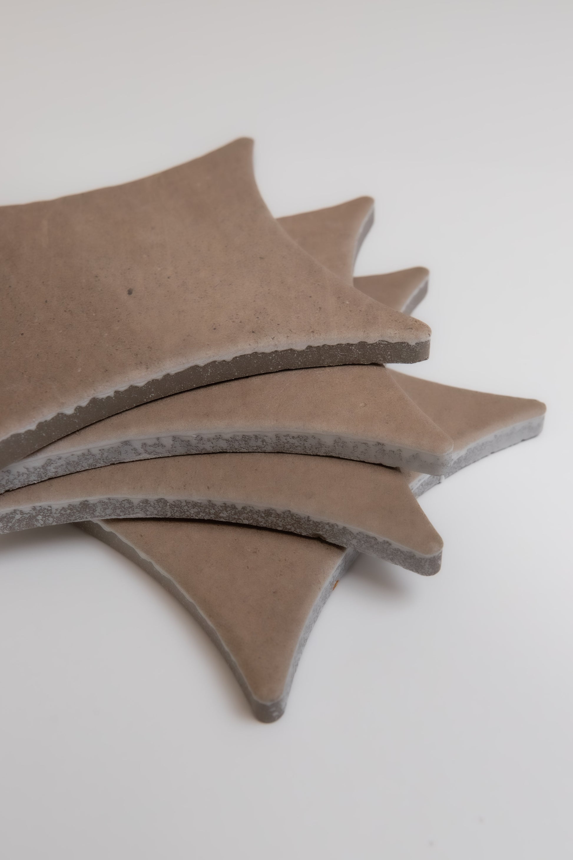 Four tan Pampas tiles by Finca, with curved shapes and rough edges, are stacked on a white surface.