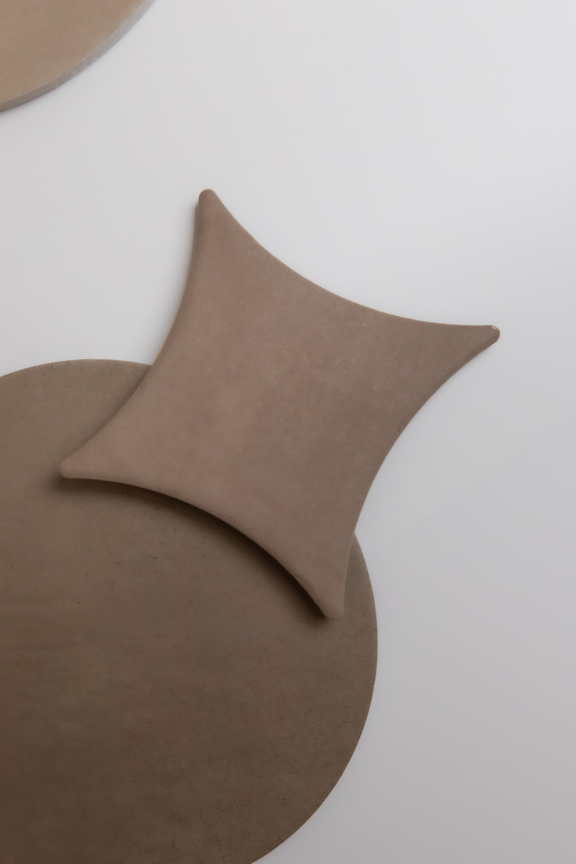 The Finca Pampas: a square tan cushion overlaps a round tan mat on a light gray surface, seen from above.