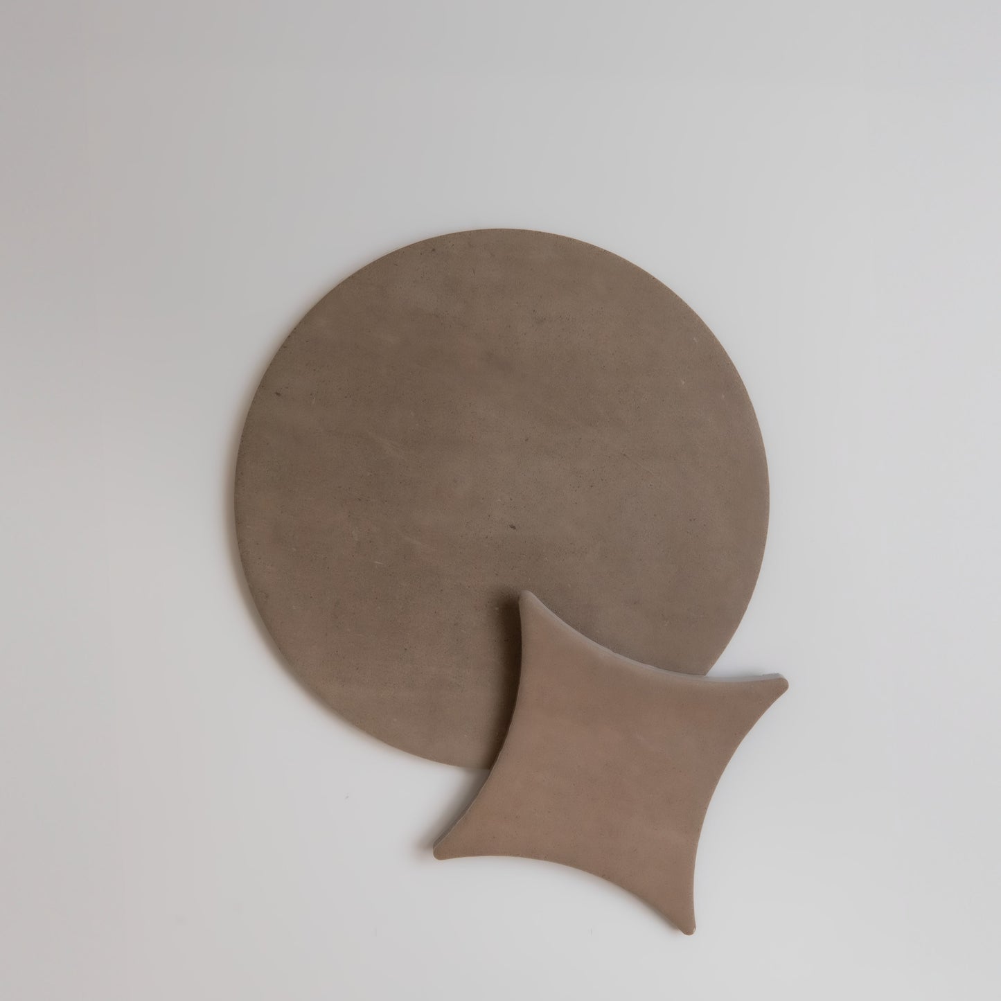 Finca Pampas: A round, flat brown object overlapped by a smaller curved square, shown on a white background.