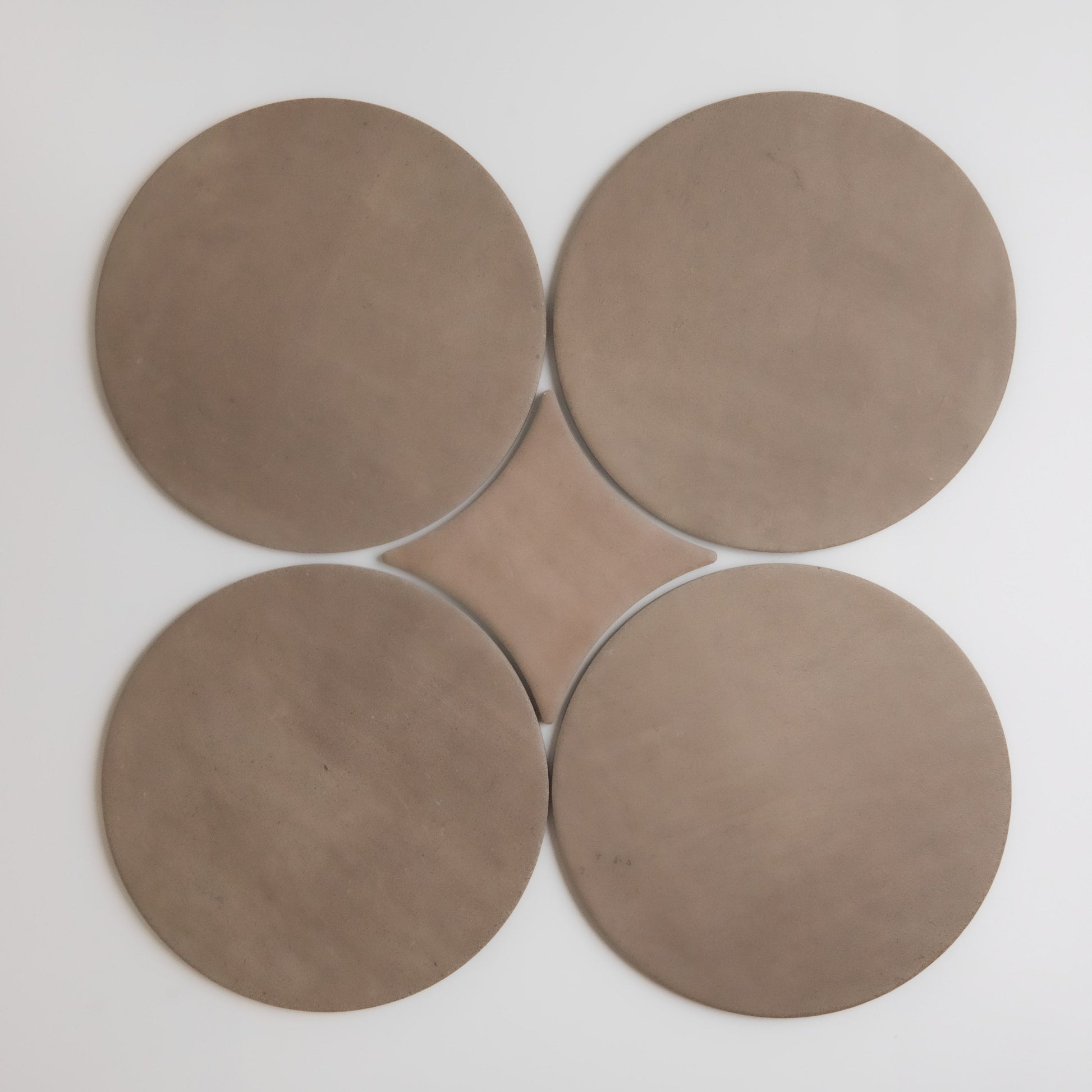 Four large, round, brown Pampas disks by Finca form a flower-like shape when arranged in a square with edges touching.