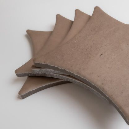 Four curved Pampas tiles by Finca in brown ceramic are stacked diagonally on a white background.