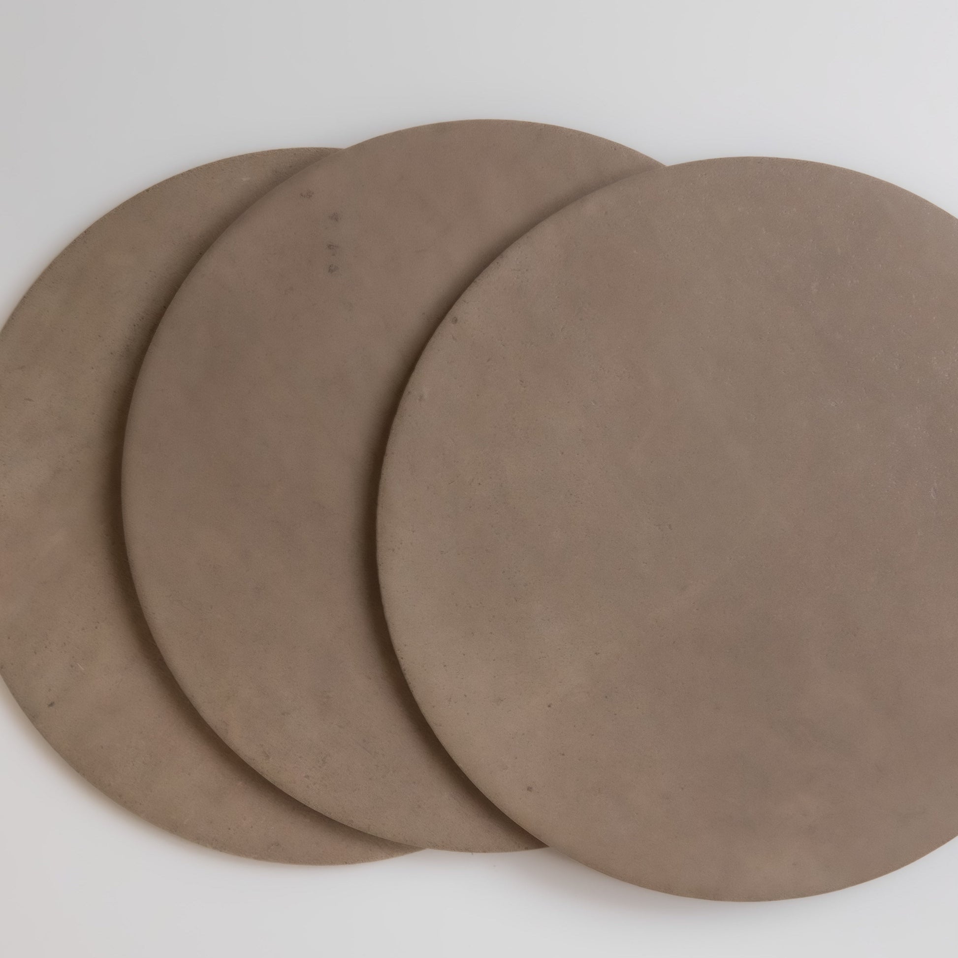 Three overlapping round brown Pampas clay slabs by Finca on a white surface, viewed from above.