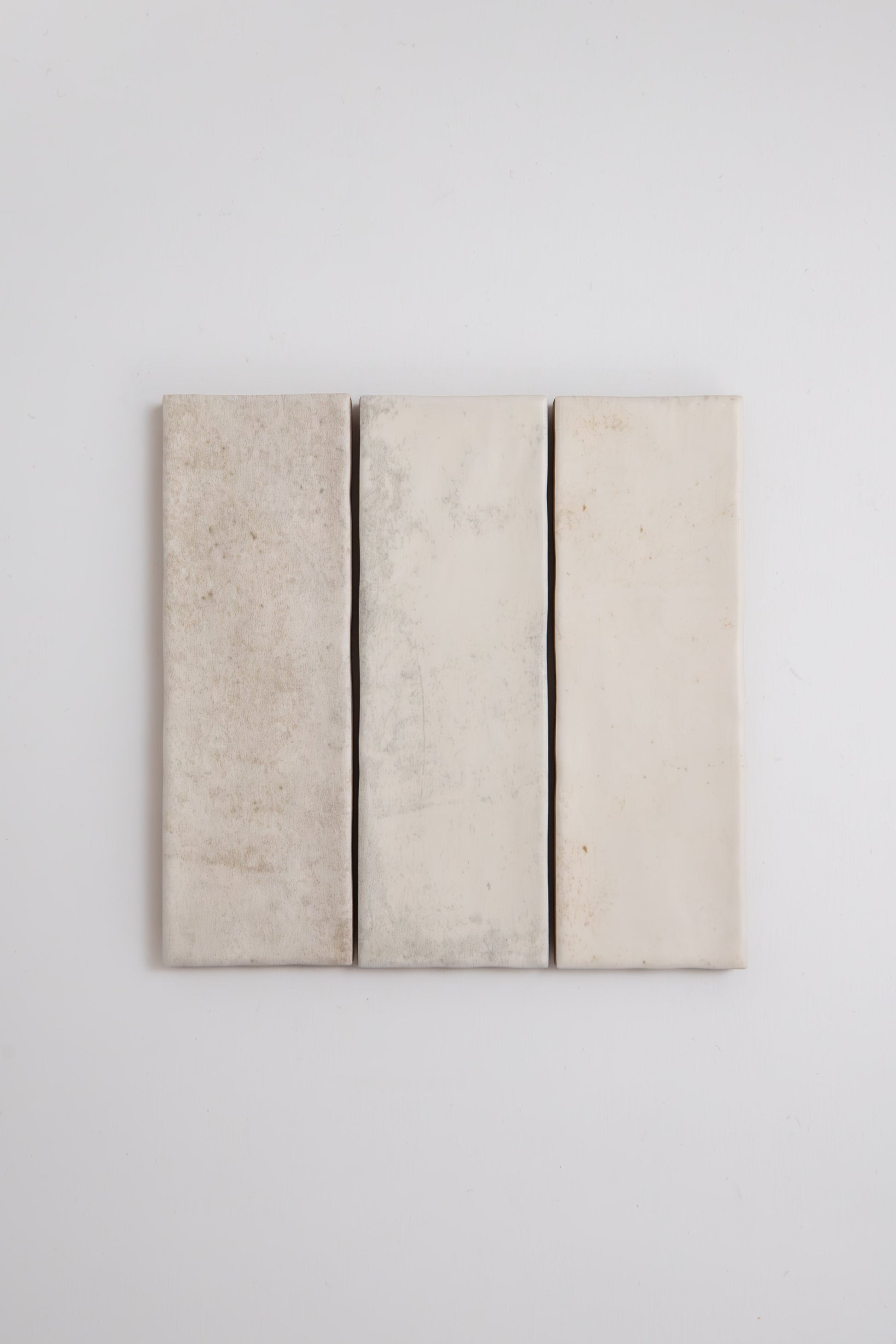 Three vertical Snowshill White Extra Sample tiles by Cottage Ivy, off-white with slight texture on a plain white wall.