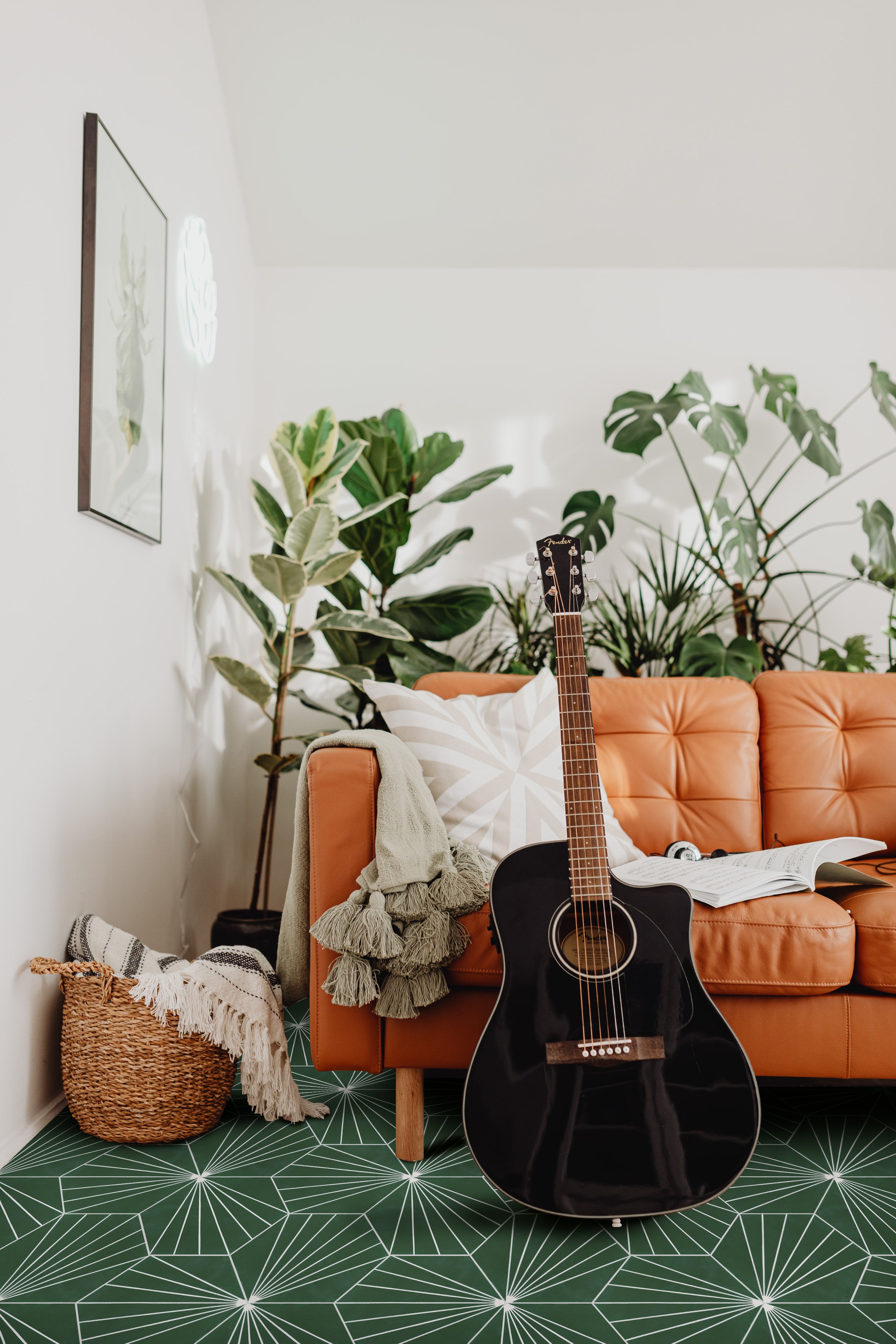 A black acoustic guitar rests against an orange sofa with green plants and a patterned rug in a cozy living room.