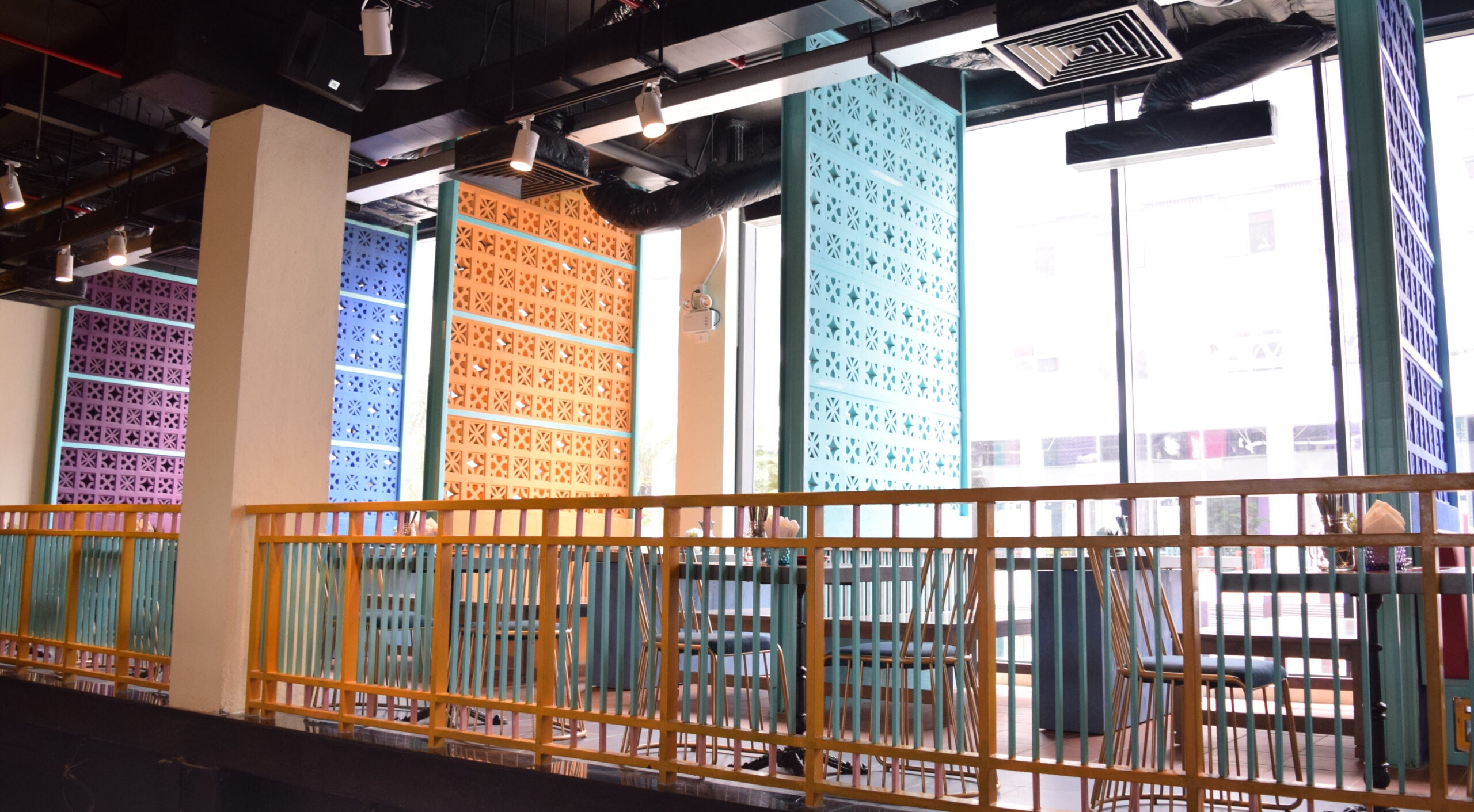Sam cement tiles by New York Cement Tile add color to a restaurant with yellow railings, blue chairs, and large windows.