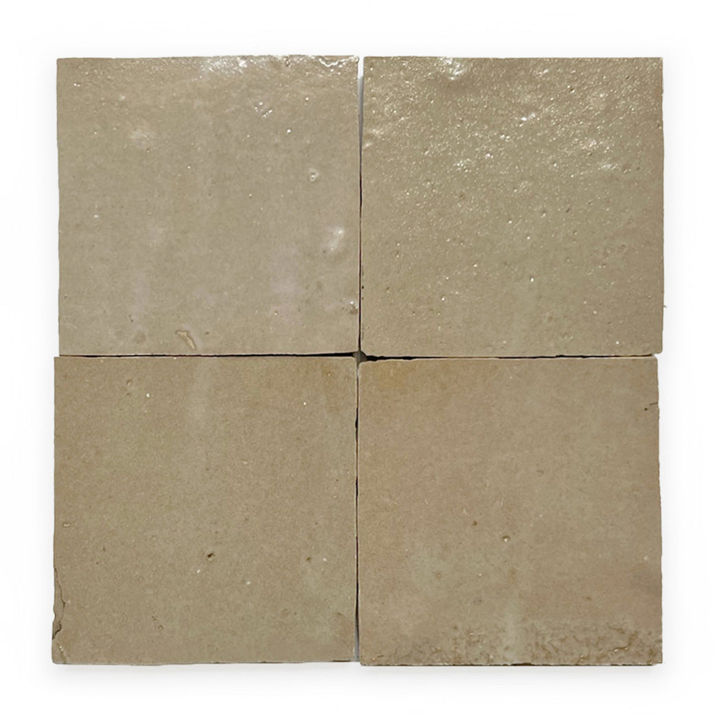 Four beige square tiles arranged in a grid, each with a slightly uneven, glossy surface and subtle texture variations.