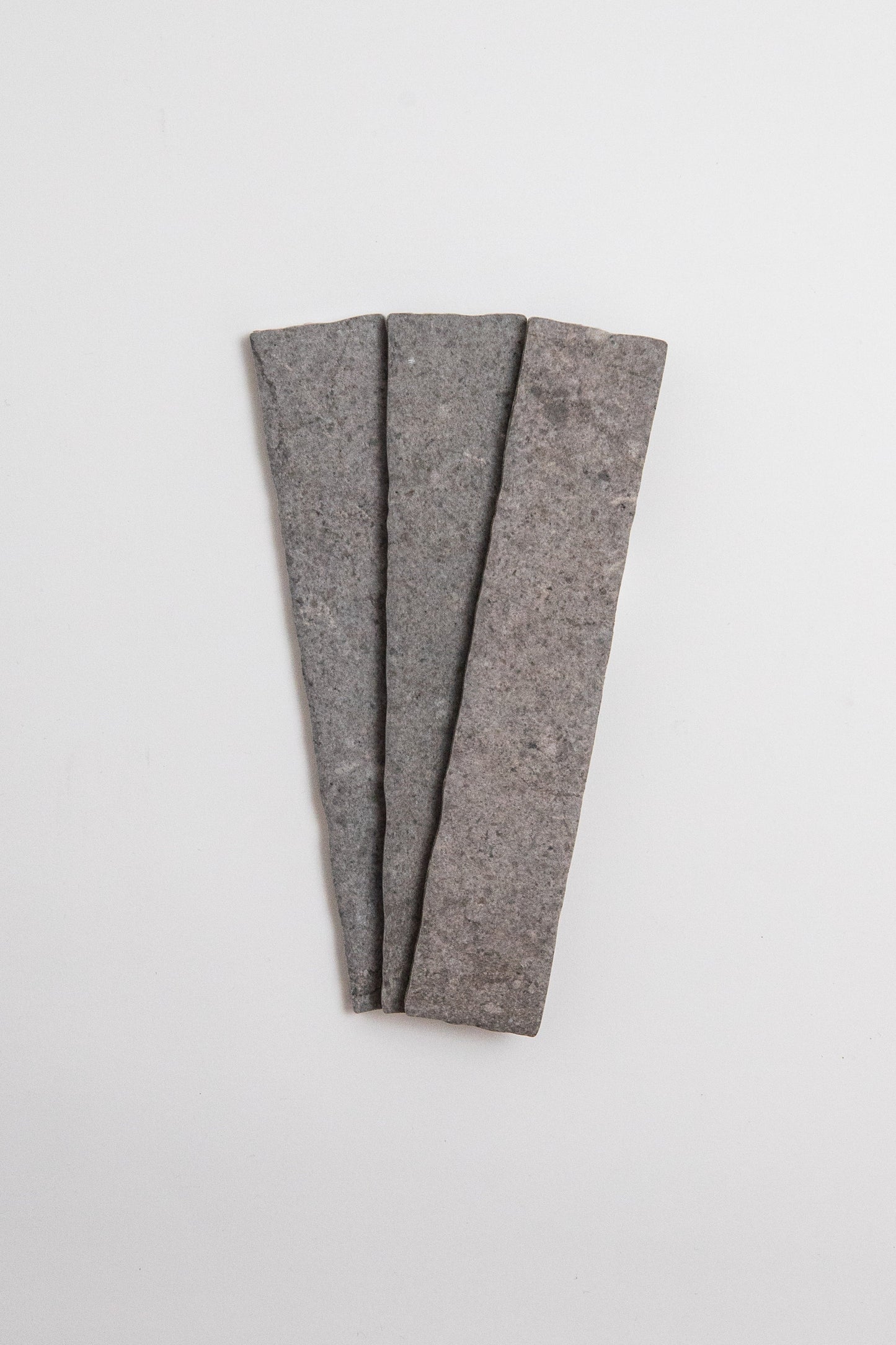 Three Toba Basilica R11 sample tiles by Toba, rectangular and gray, arranged fan-shaped on a white background.