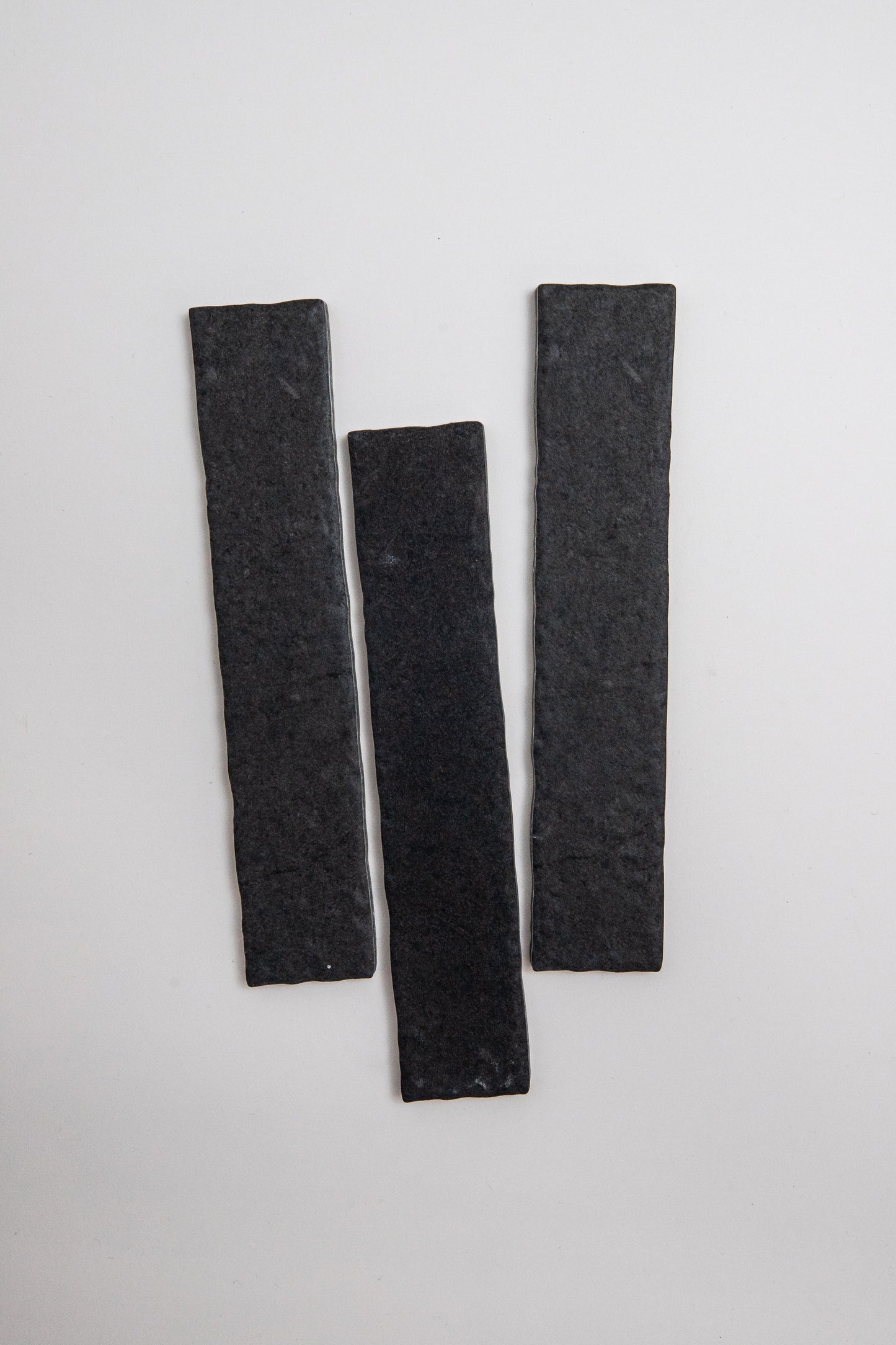 Three Toba Black R11 sample tiles, rectangular and dark gray, are arranged vertically on a plain light background.