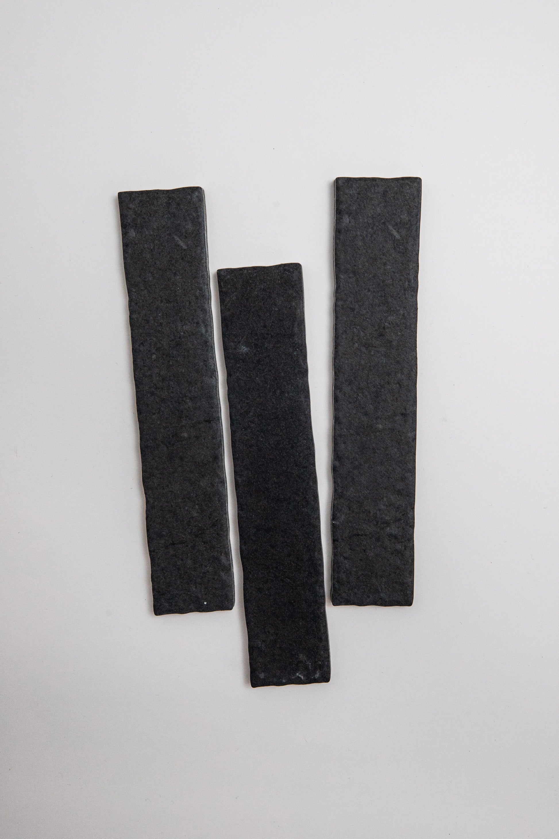 Three Toba Black R11 sample tiles, rectangular and dark gray, are arranged vertically on a plain light background.