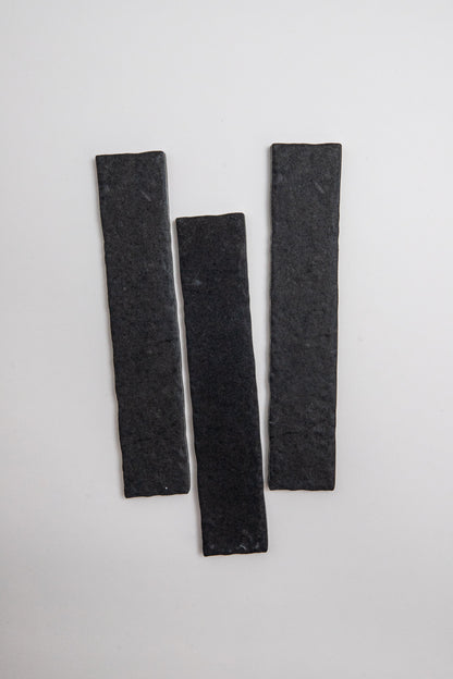 Three Toba Black R11 sample tiles, rectangular and dark gray, are arranged vertically on a plain light background.