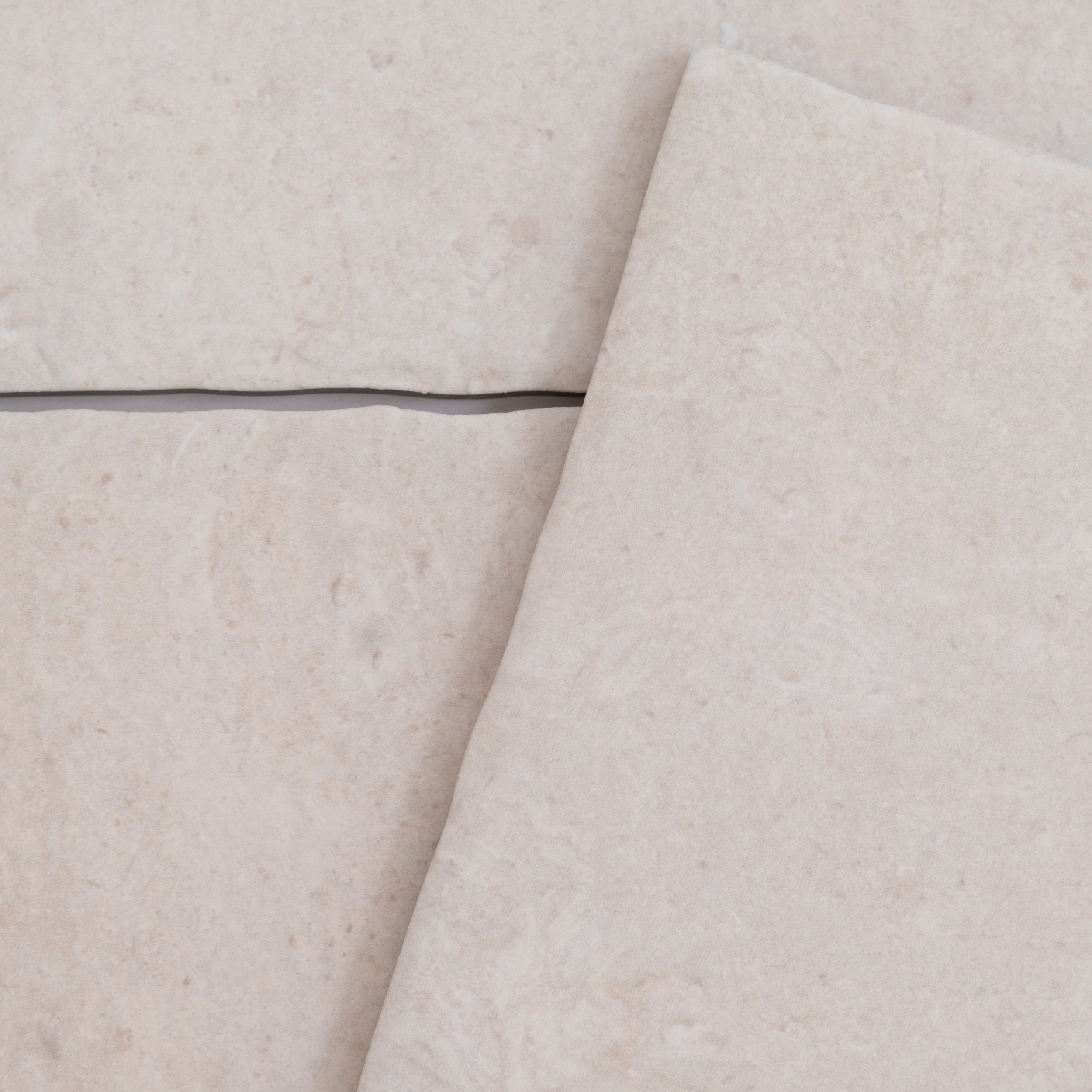 Close-up of Toba Ivory R11 tiles by Toba, in light beige with a visible grout line and slight tile overlap.