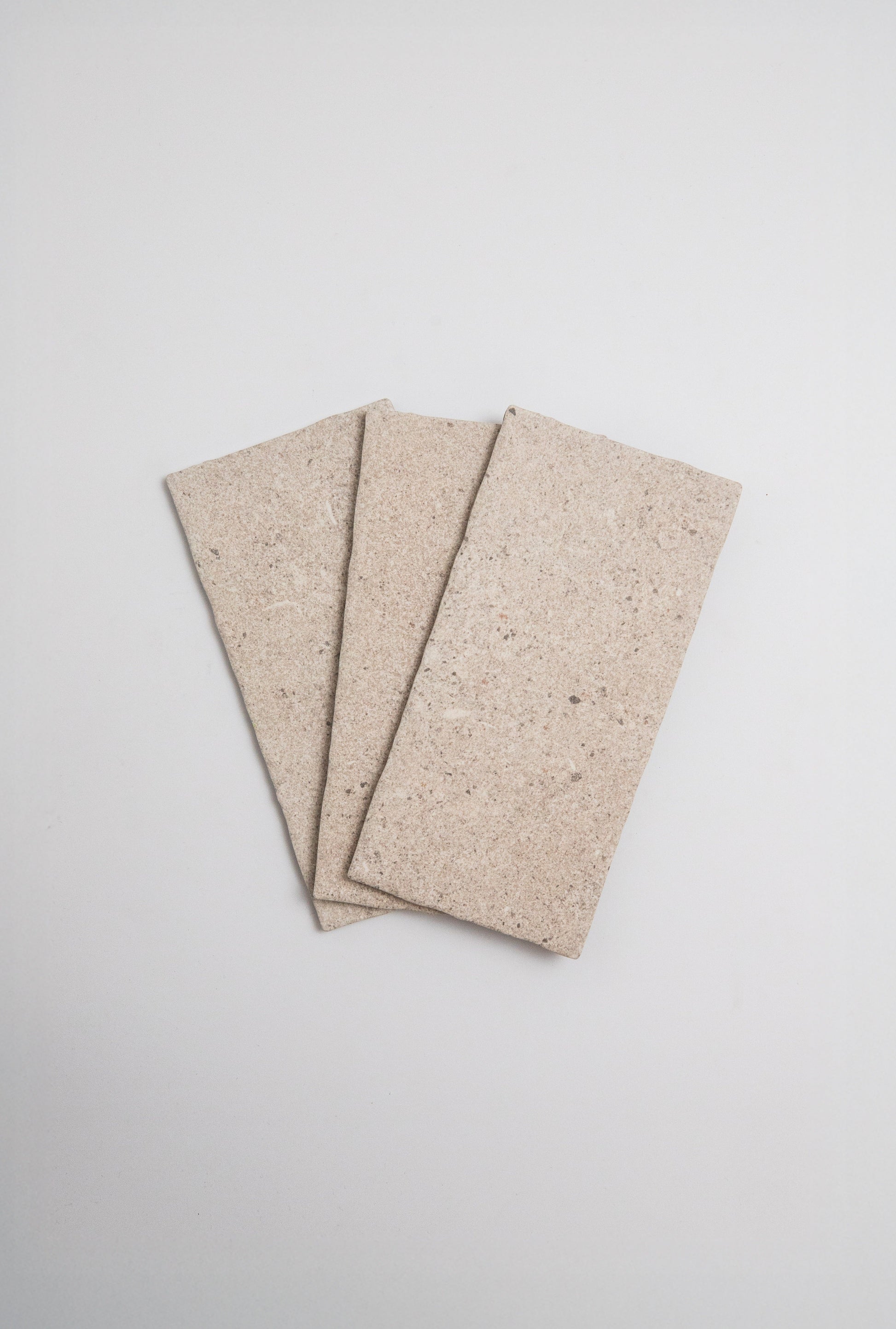 Three Toba Taupe R11 sample tiles by Toba displayed in a fan shape on a plain light background.