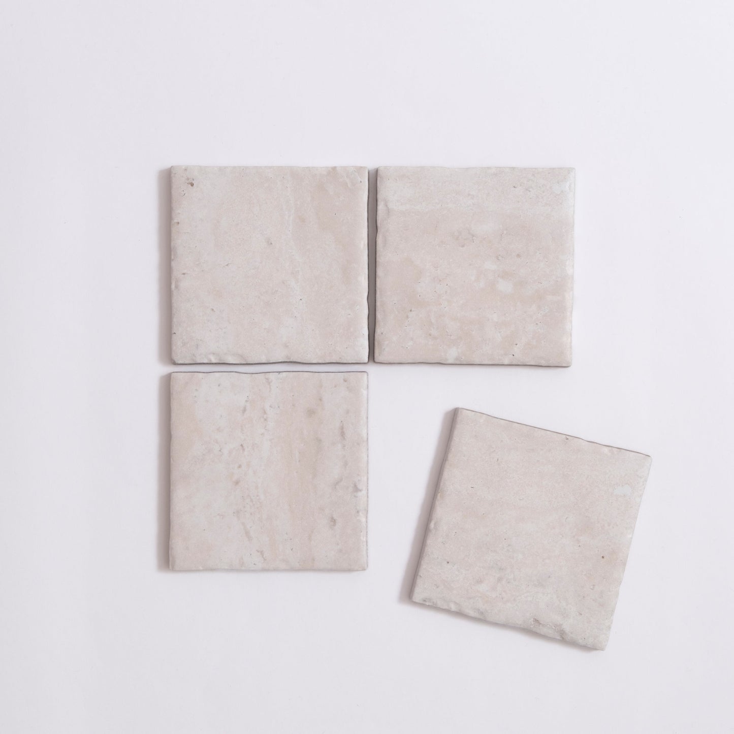 Four Tosca Travertine light beige square tiles, three aligned with one slightly askew, on a white background.