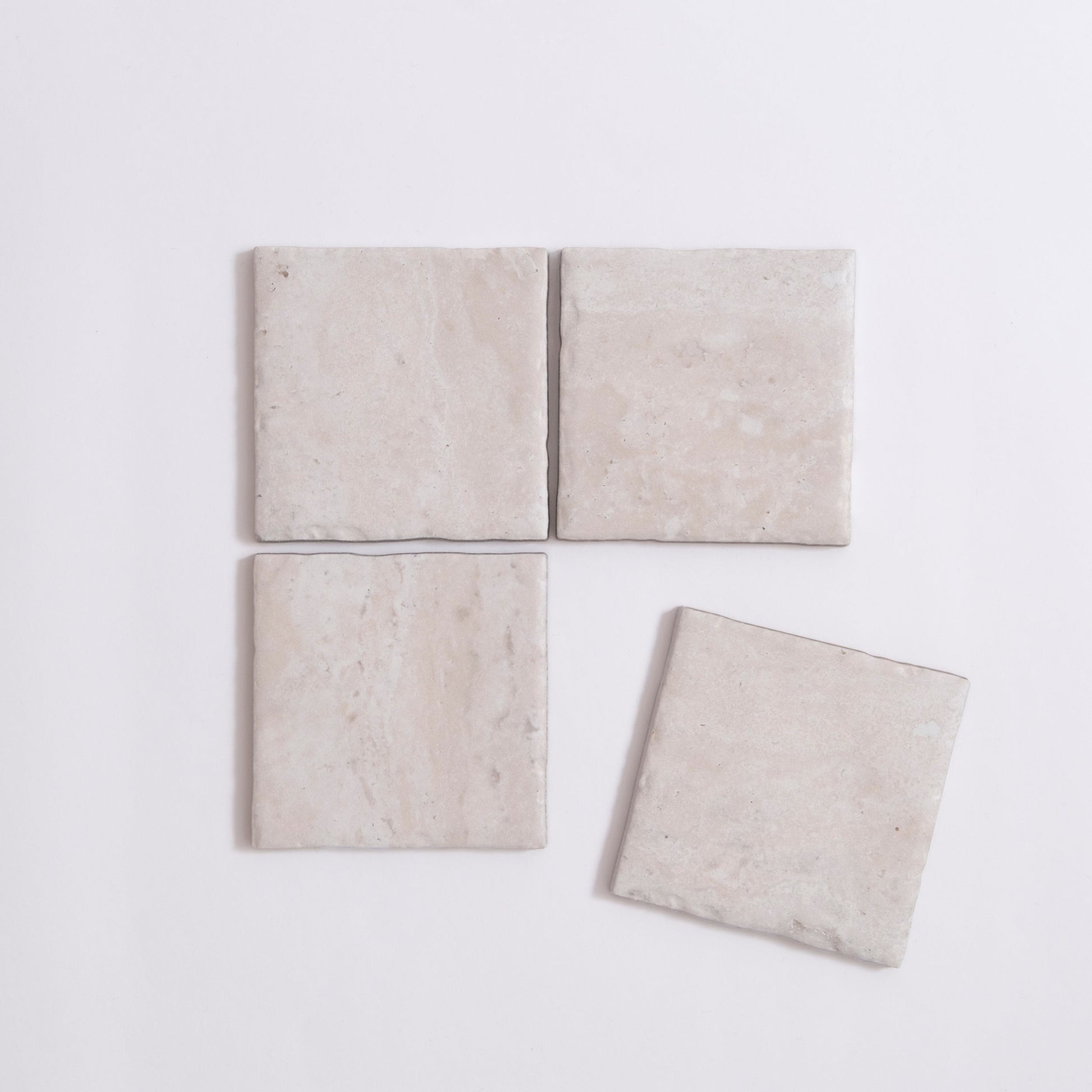 Four Tosca Travertine light beige square tiles, three aligned with one slightly askew, on a white background.