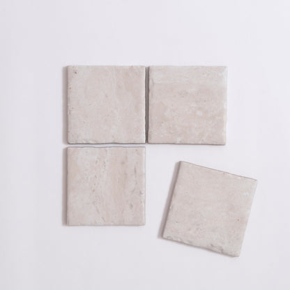 Four Tosca Travertine light beige square tiles, three aligned with one slightly askew, on a white background.