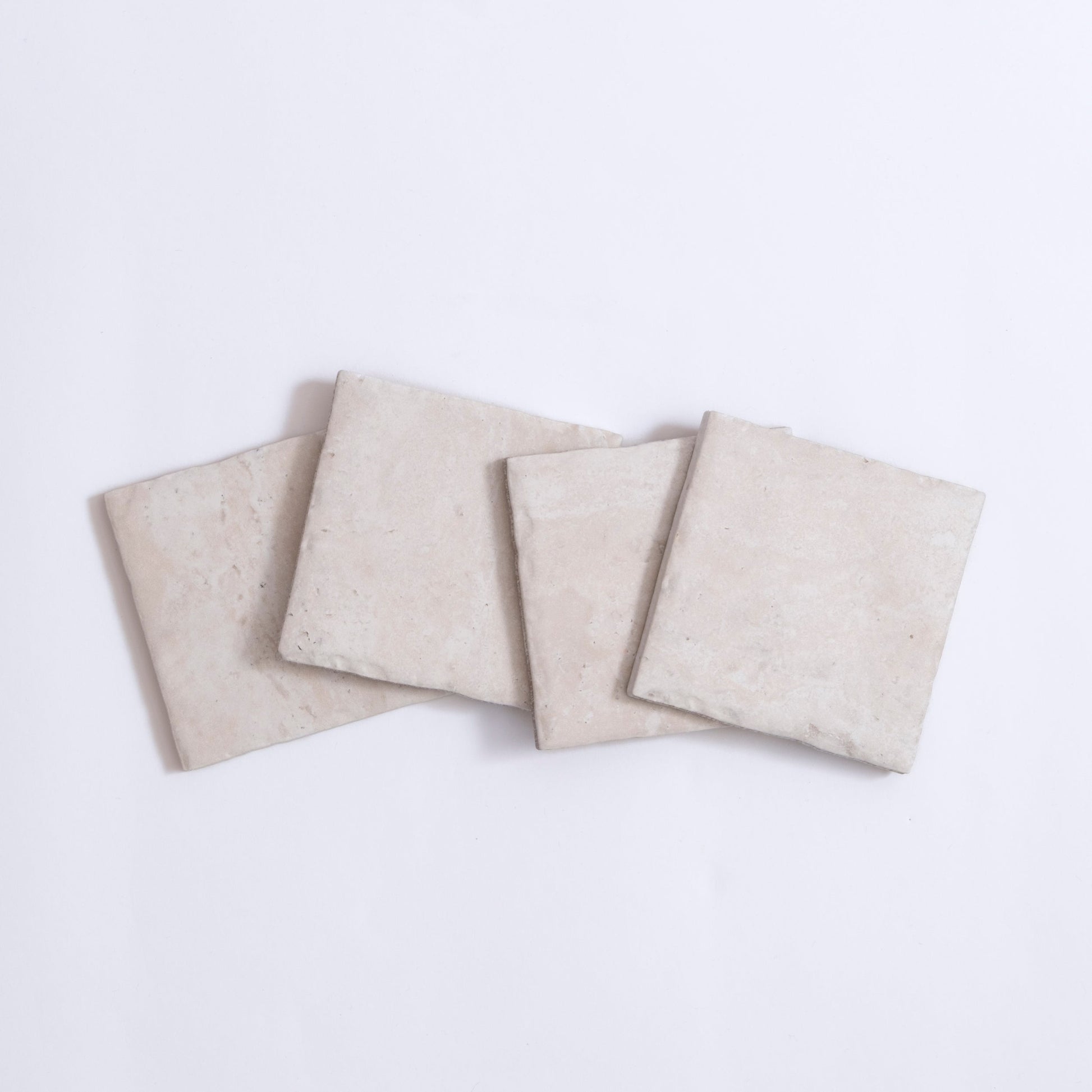 Four Tosca Travertine tiles in light beige are arranged in a slightly overlapping row on a white background.