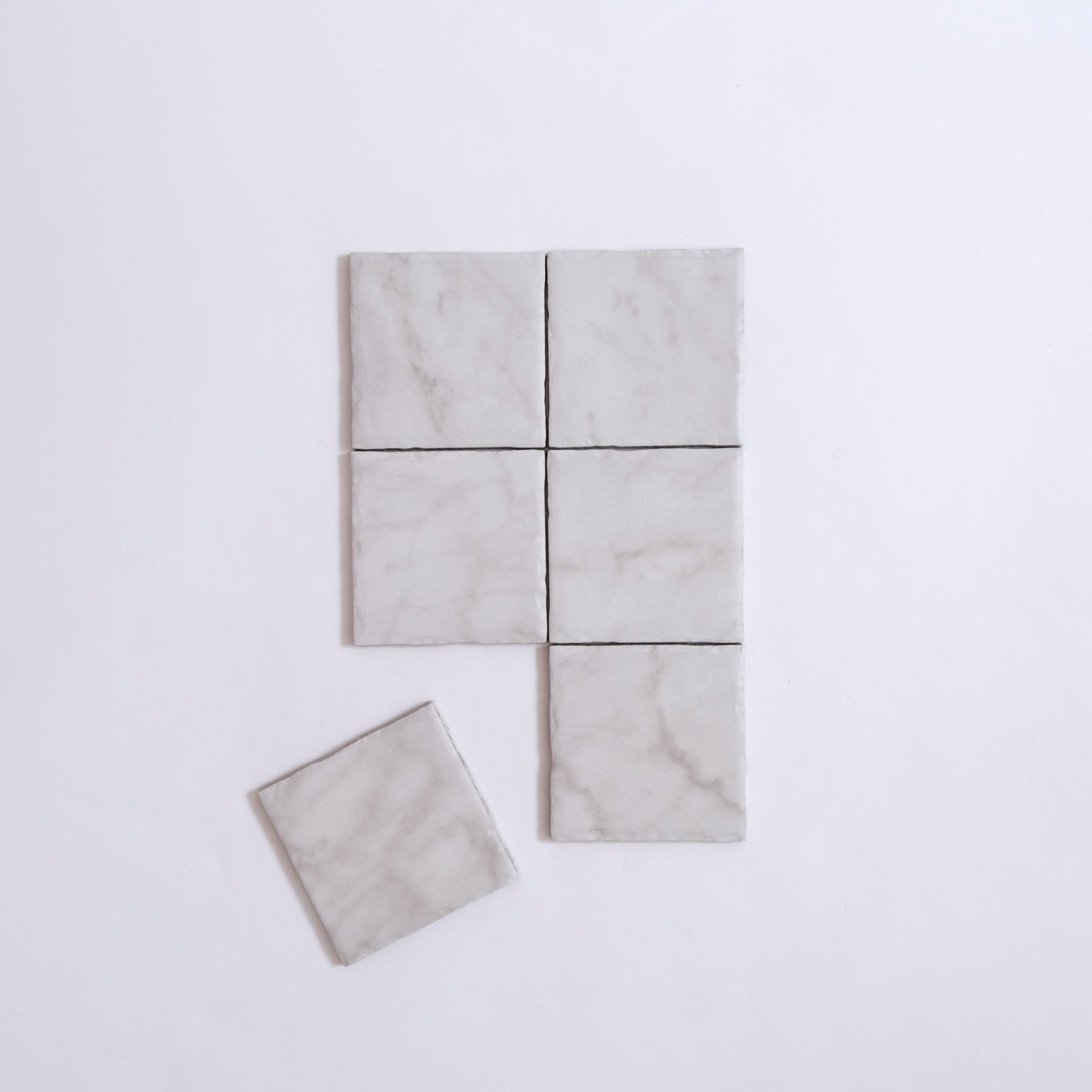 Five Tosca White Carrara Extra marble tiles on a white surface, one tile set slightly apart from the rest.
