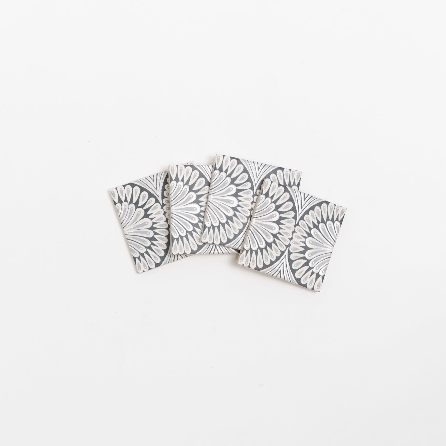 Four Zoe Deco coasters by Cottage Ivy, with a black & white geometric floral pattern, arranged in a fan shape.