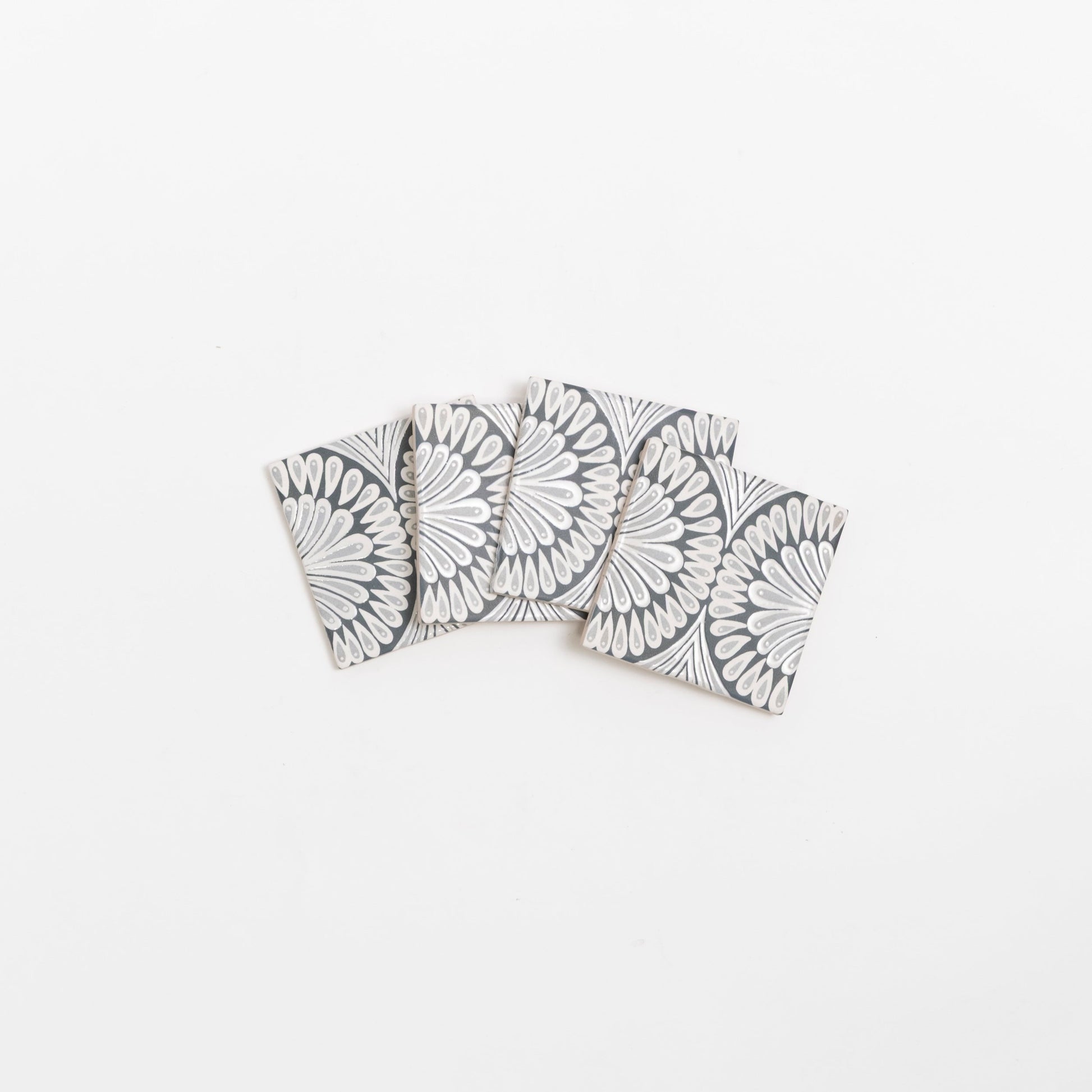 Four Zoe Deco coasters by Cottage Ivy, with a black & white geometric floral pattern, arranged in a fan shape.